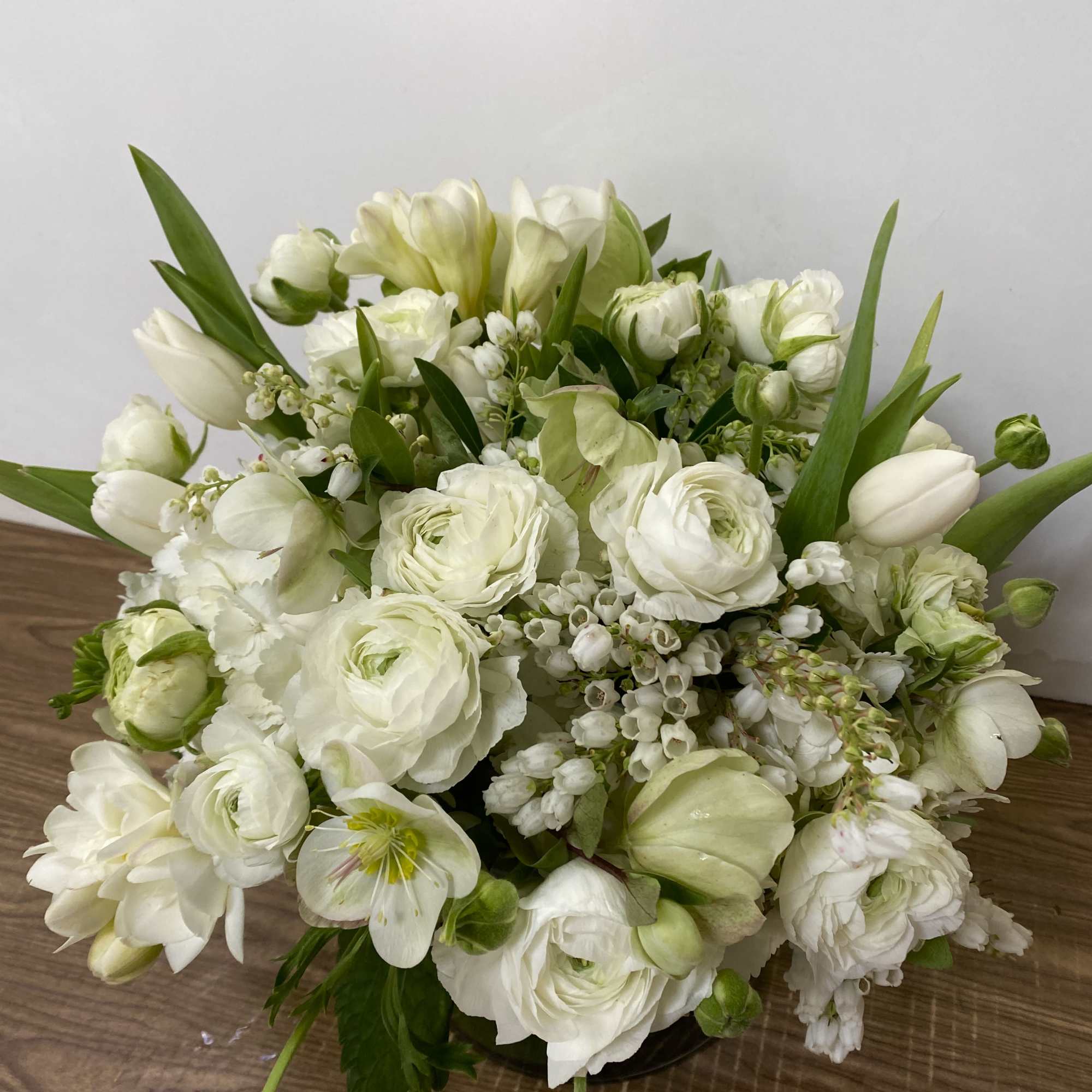 White Hydrangea, tulips, ranunculus in 
a clear glass vase.