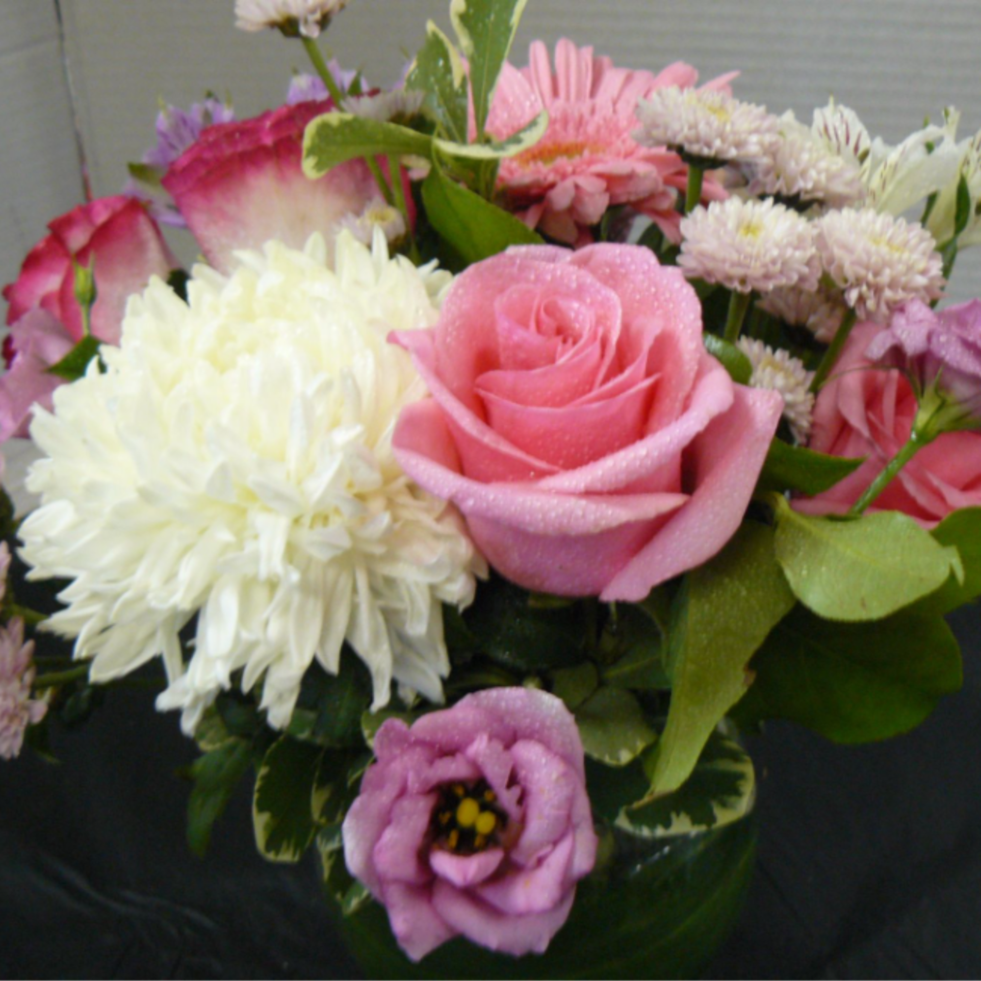 Low glass vase of pink roses, lavender lisianthus, white mum, and mixed pink daisies
