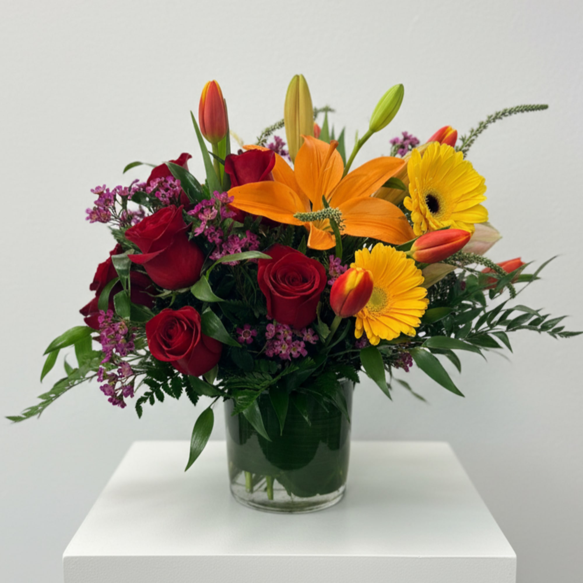 Colorful arrangement of red roses, orange lilies, and yellow gerbera daisies in a clear glass vase