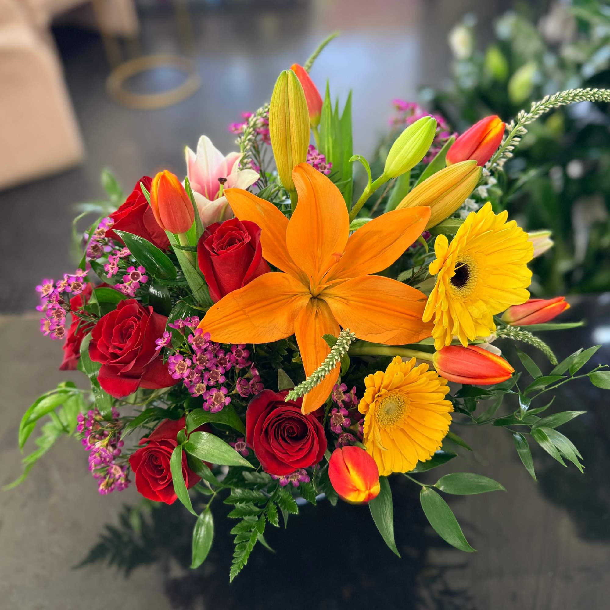 Bright mixed bouquet with an orange lily, yellow gerbera daisies, red roses, tulips, and small purple blooms