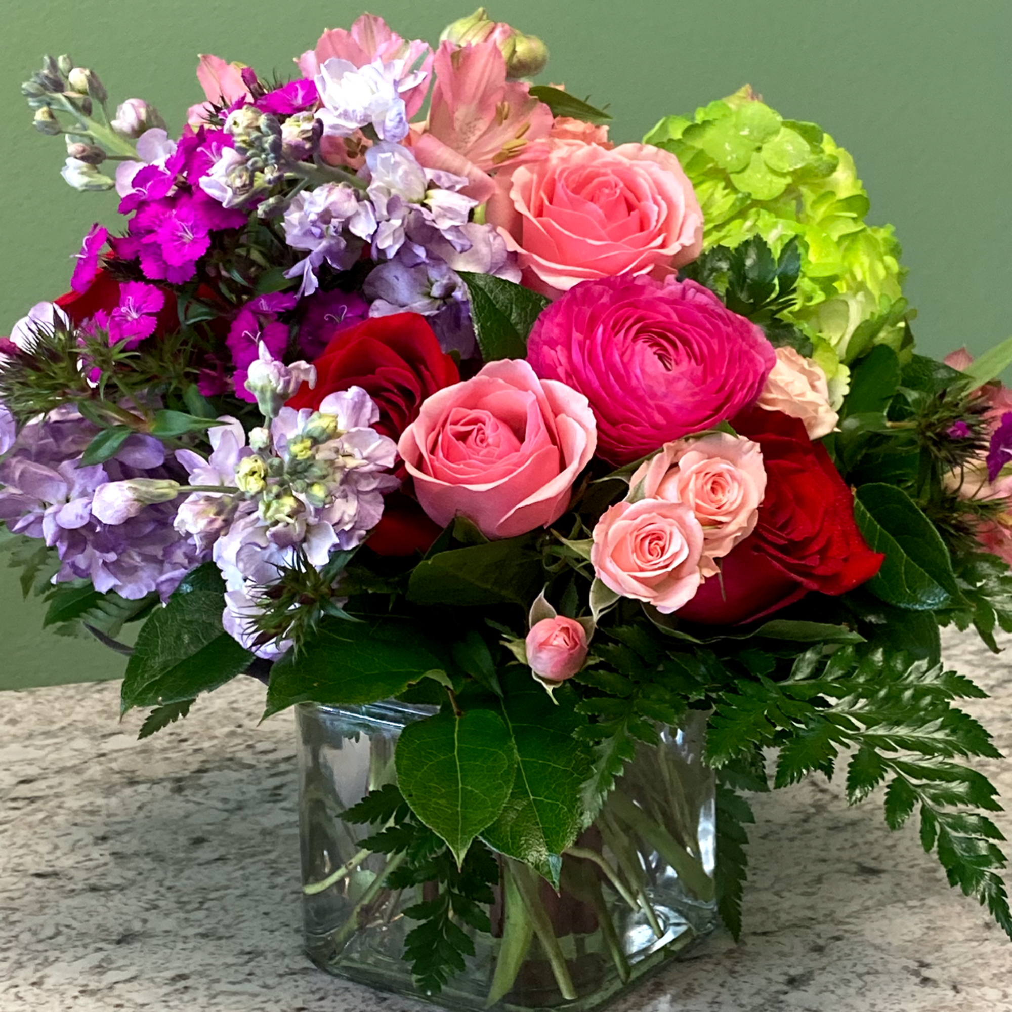 Mixed bouquet of pink and red roses with purple blooms in a clear glass cube vase