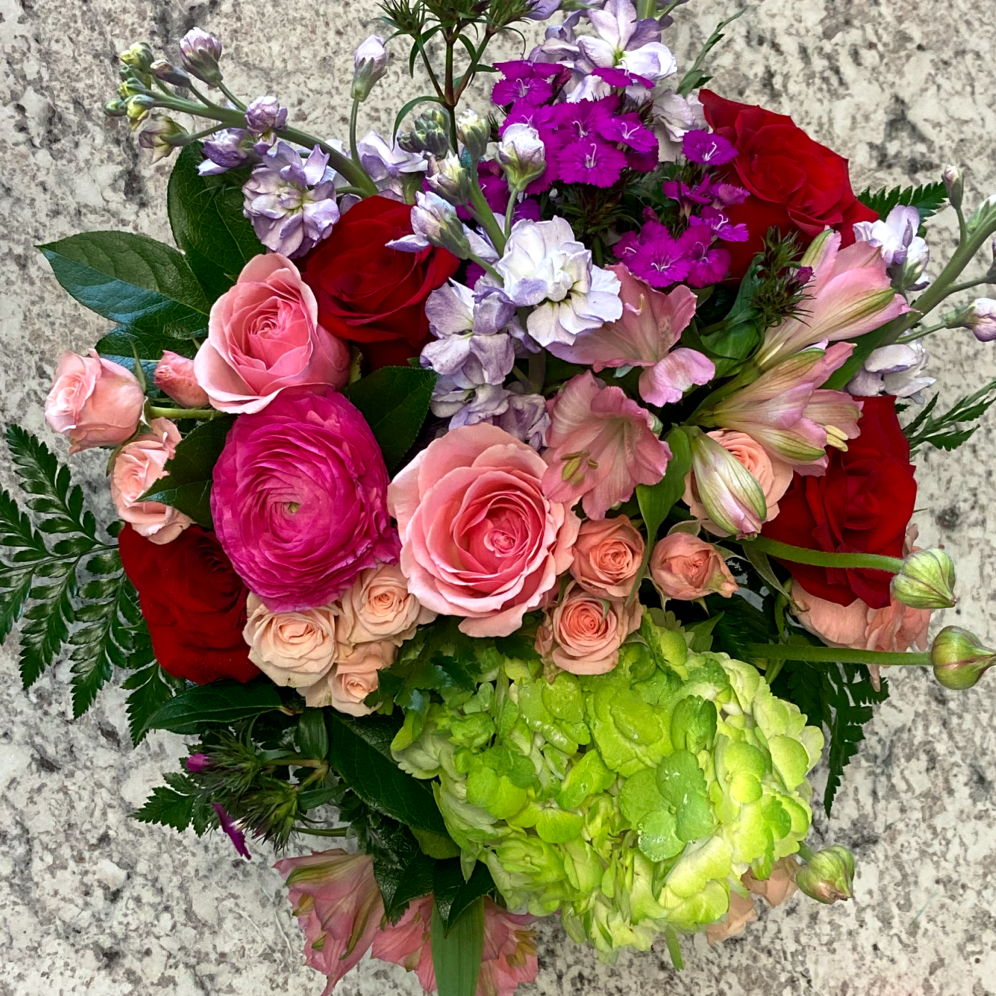 Mixed bouquet of pink and red roses, ranunculus, and green hydrangea in a glass vase