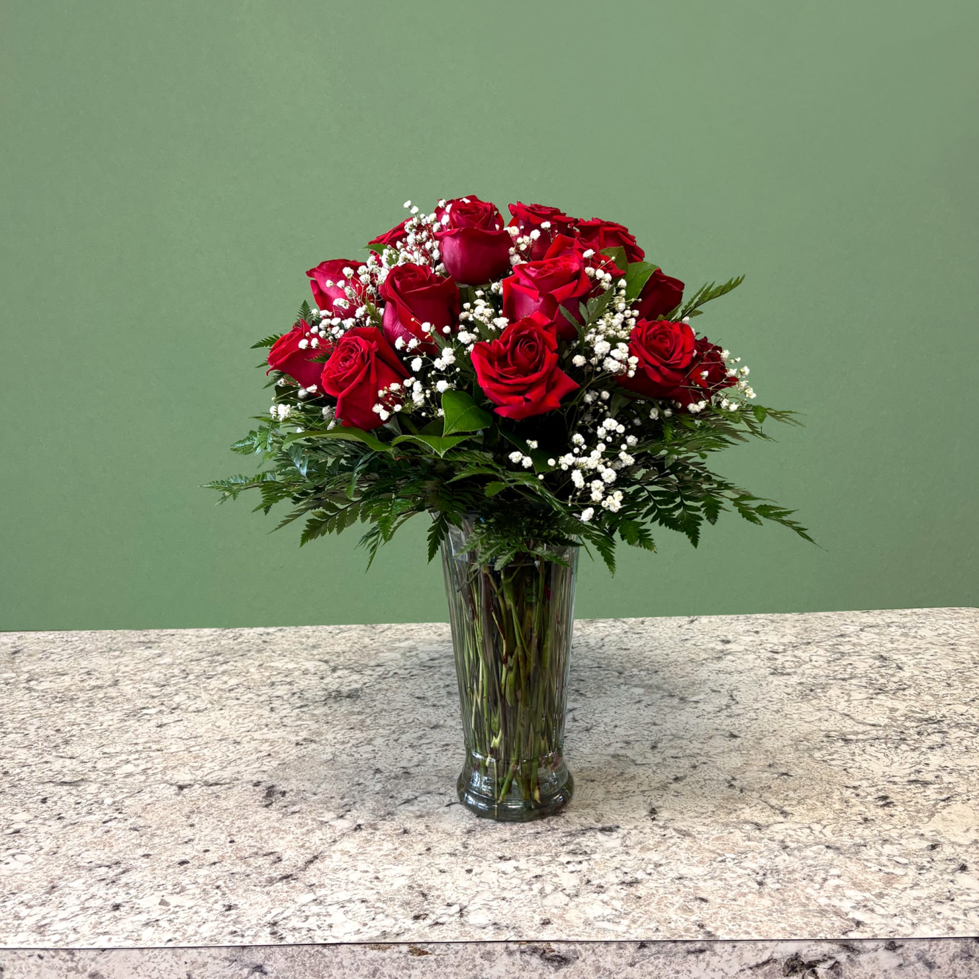 Tall clear vase of red roses with white accent flowers on a stone countertop