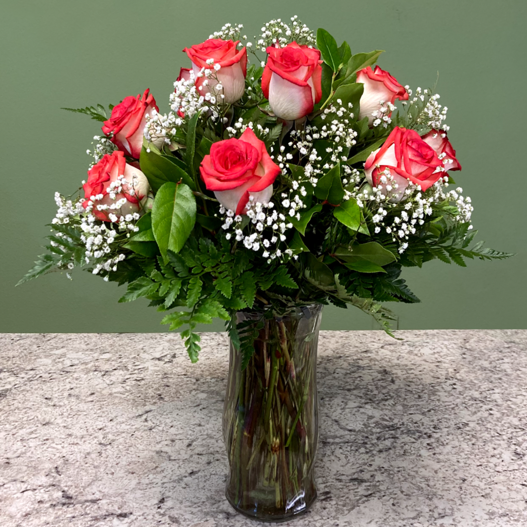 Vase arrangement of red and white roses with baby's breath in a clear glass vase on a stone countertop