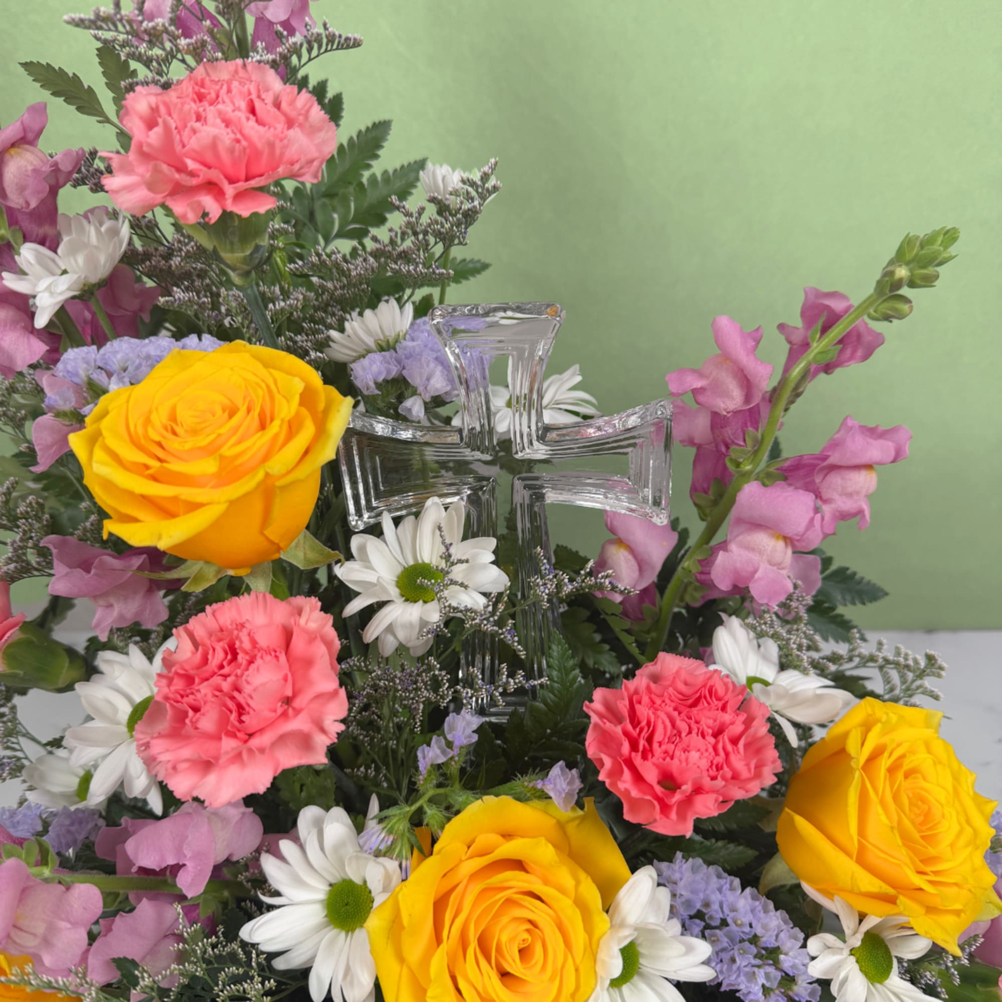 A clear glass cross nestled at the heart of softly layered blooms