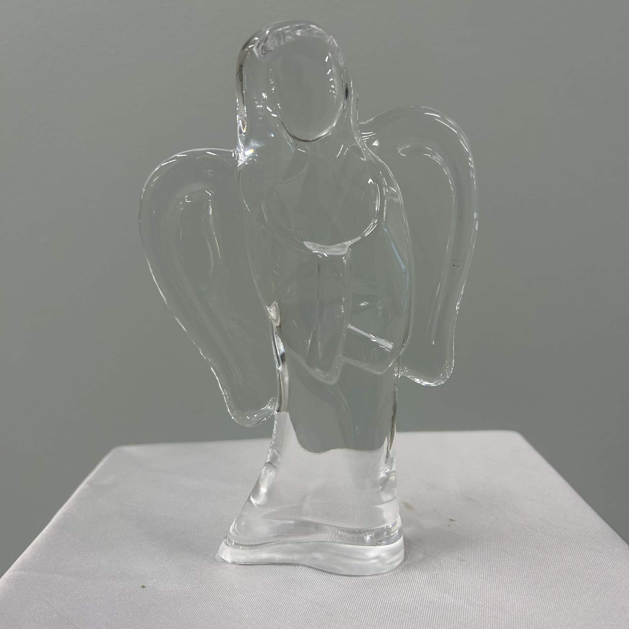 Soft pink gerbera daisies and peach-pink roses surround a clear glass angel