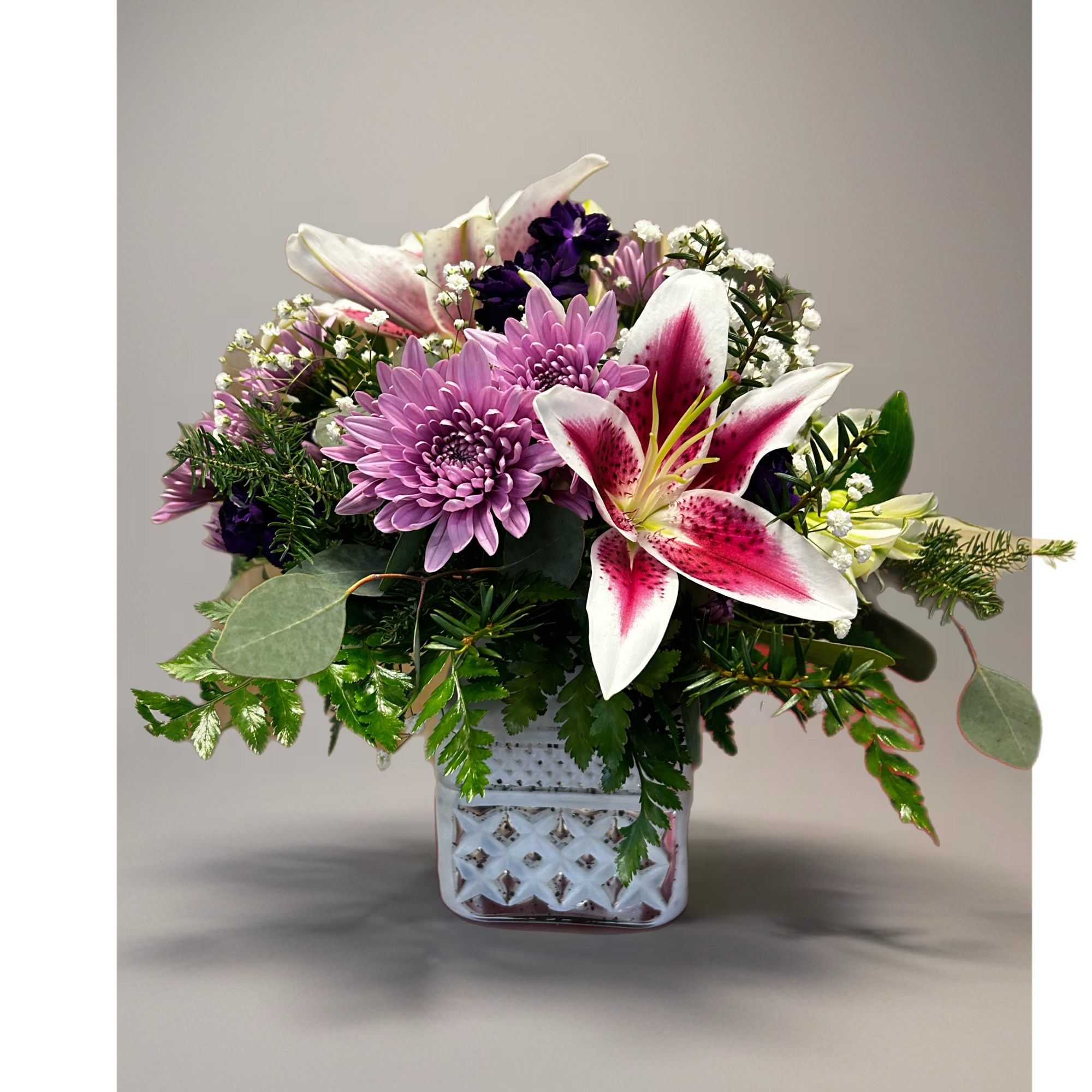 Pink lilies and lavender mums arranged with white filler flowers in a white cube vase