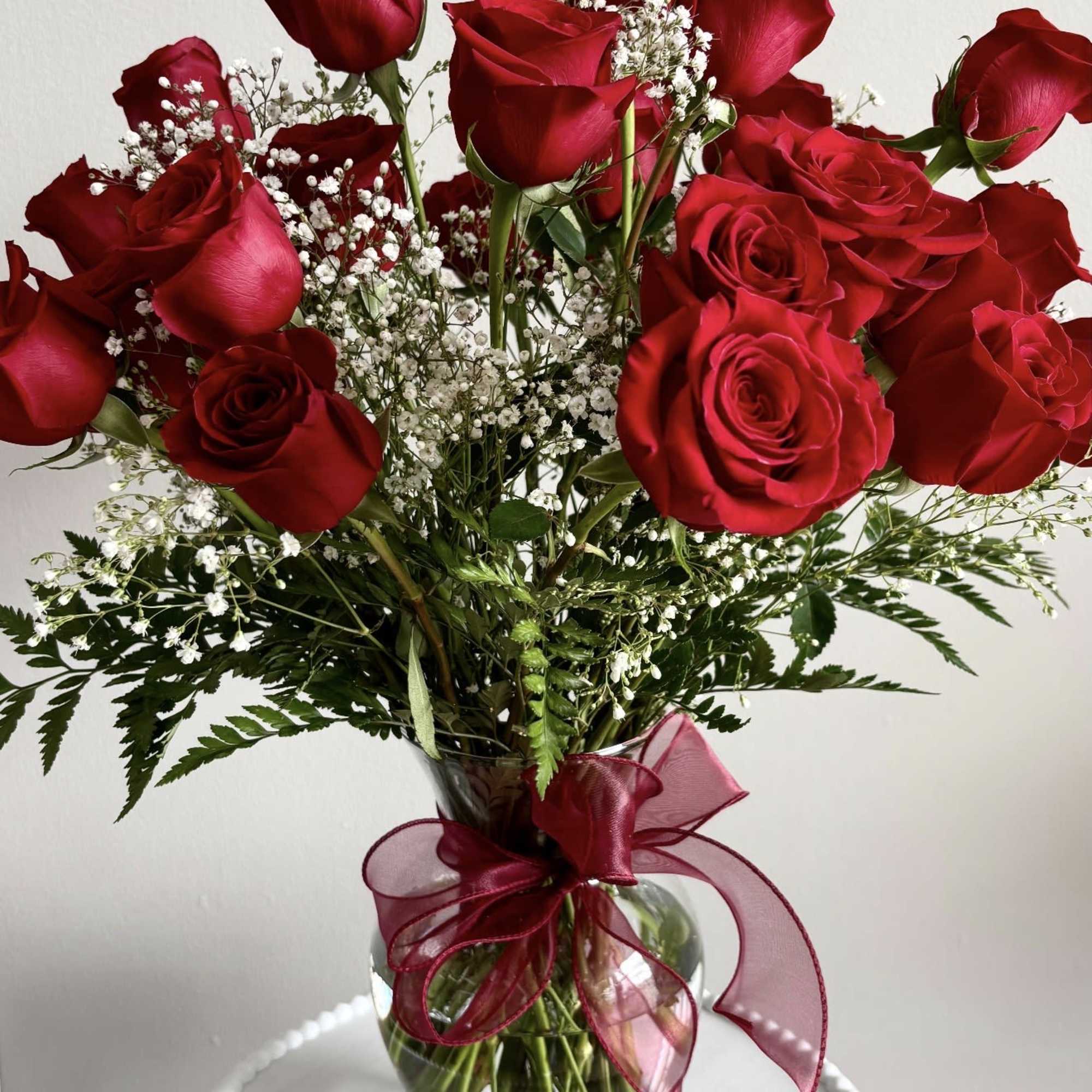 Red roses in a clear glass vase with baby's breath and a burgundy ribbon