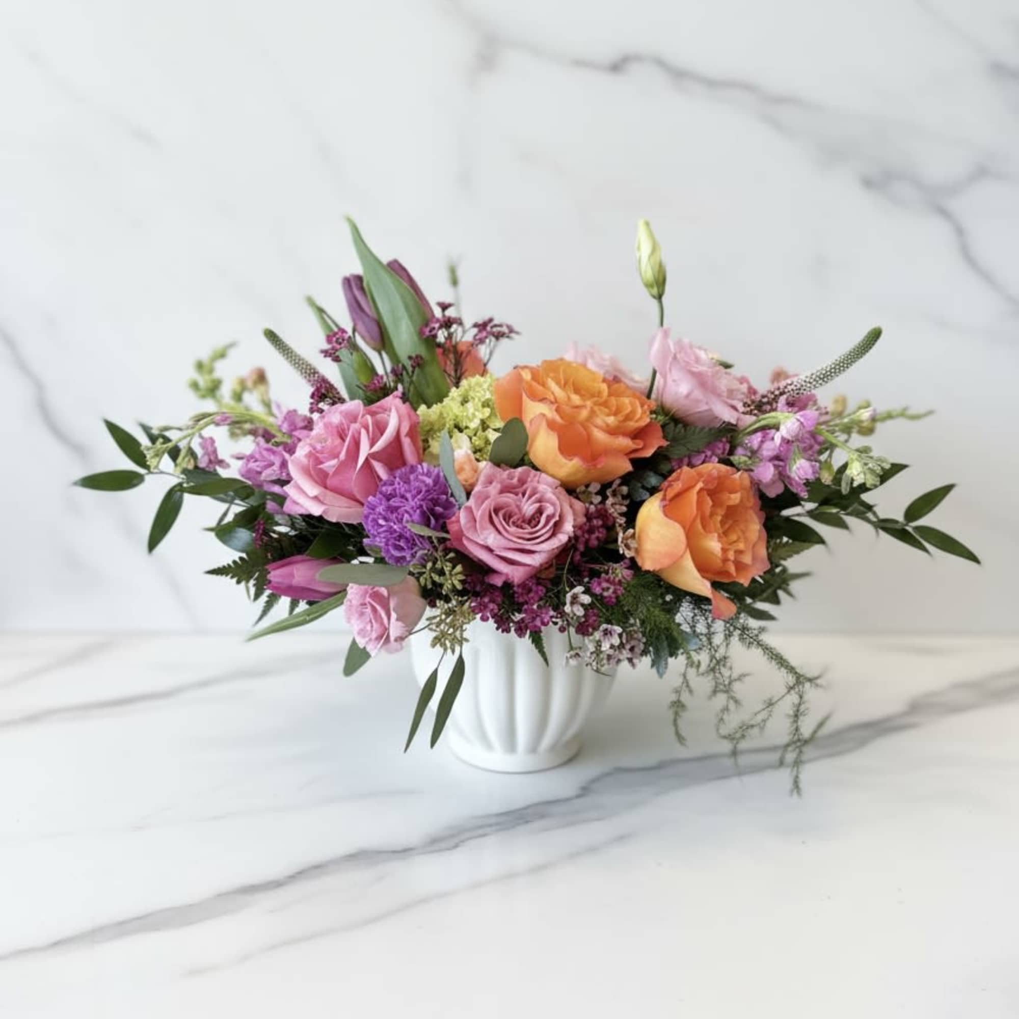 This joyful garden-style arrangement is filled with vibrant coral roses, fragrant lilac*