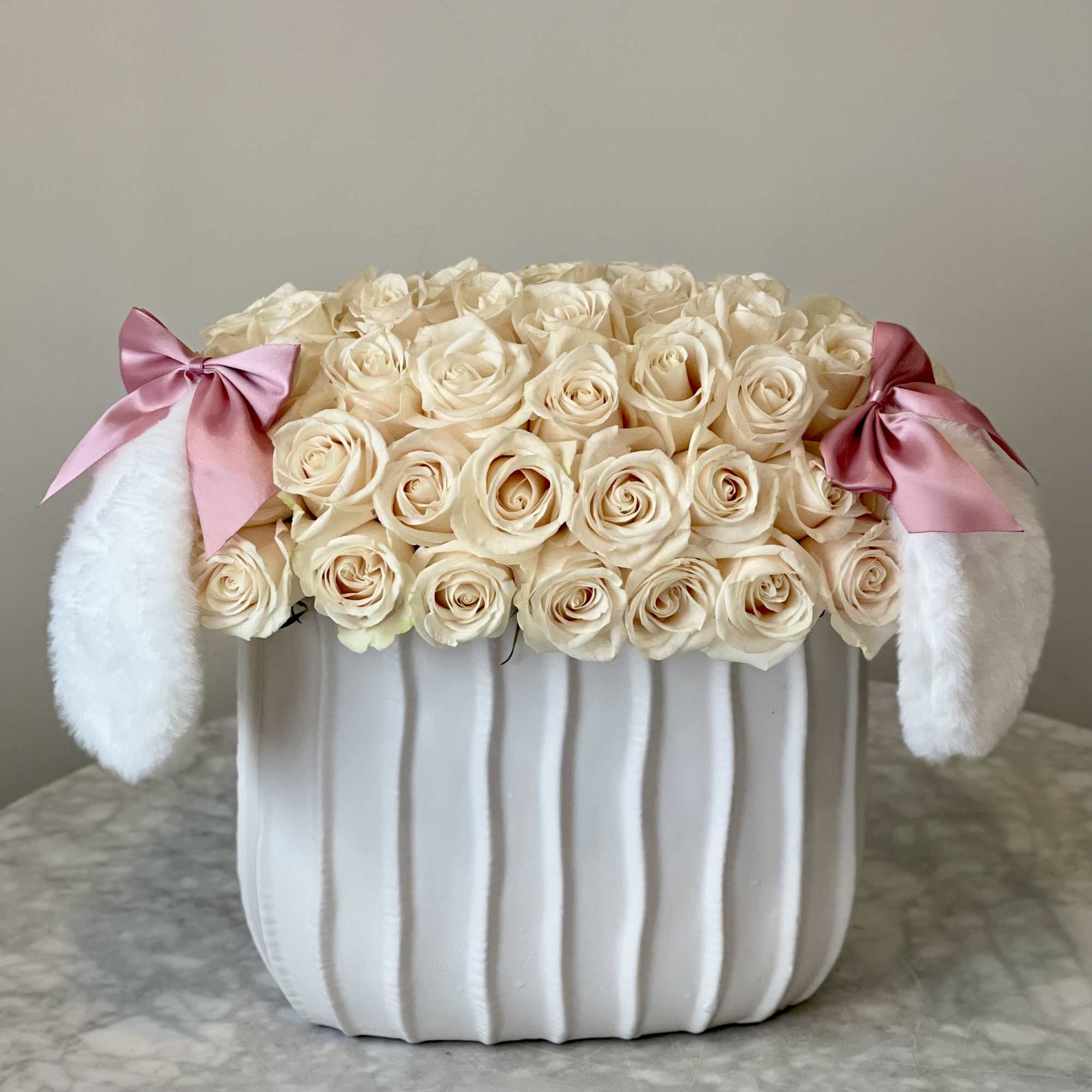 Cream roses in a white textured container with fuzzy bunny ears and pink bows