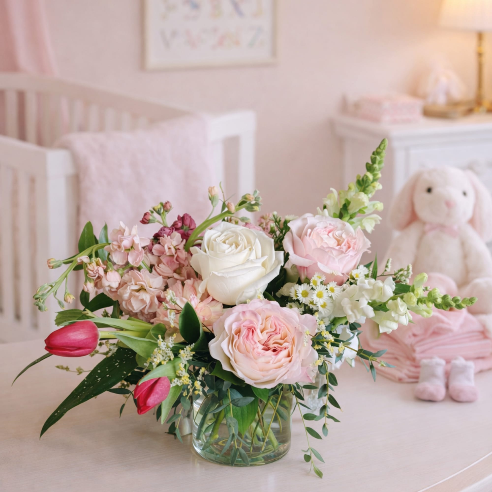 Pastel pink and white flower arrangement with roses and tulips in a clear glass vase on a nursery dresser