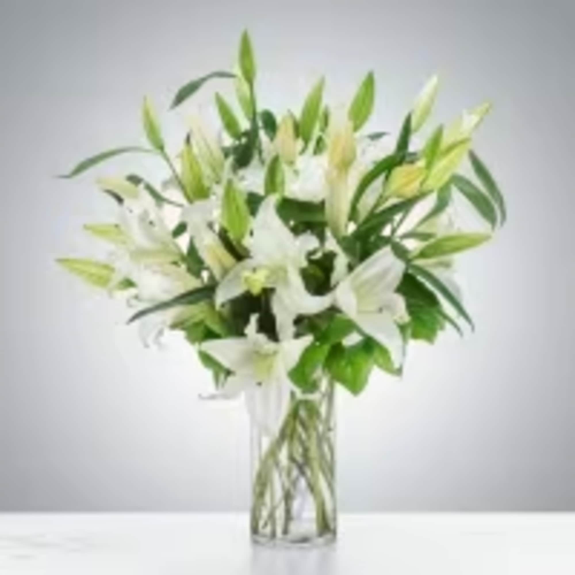 White lilies and buds arranged in a tall clear glass vase