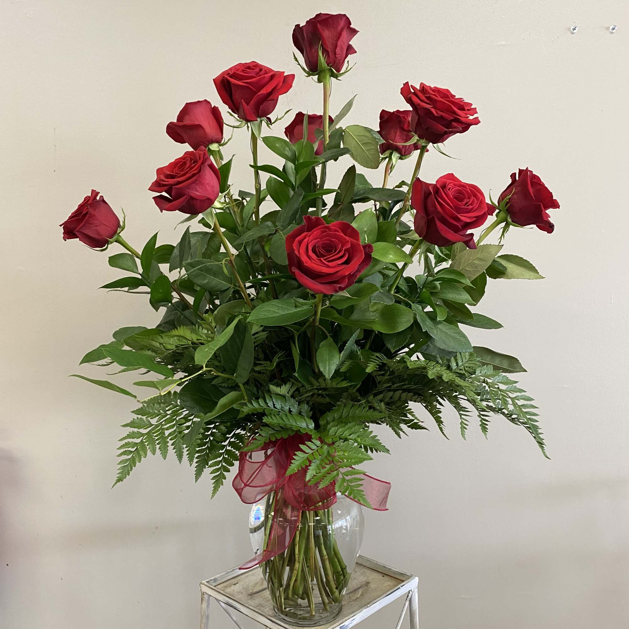 A dozen long stem red roses with assorted greenery in a clear