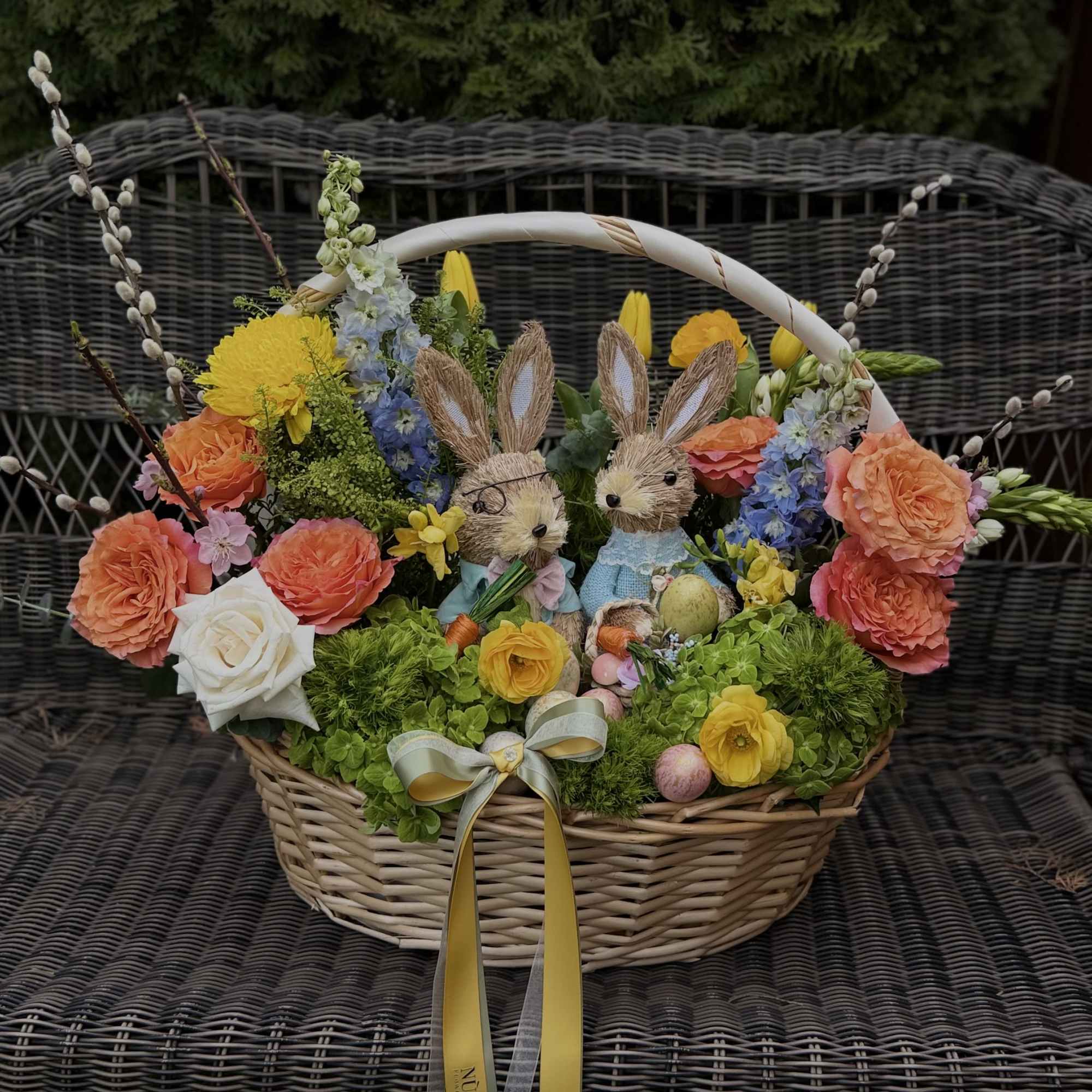 Ester basket with fresh flowers, decorative eggs and cute bunnies. Perfect Easter