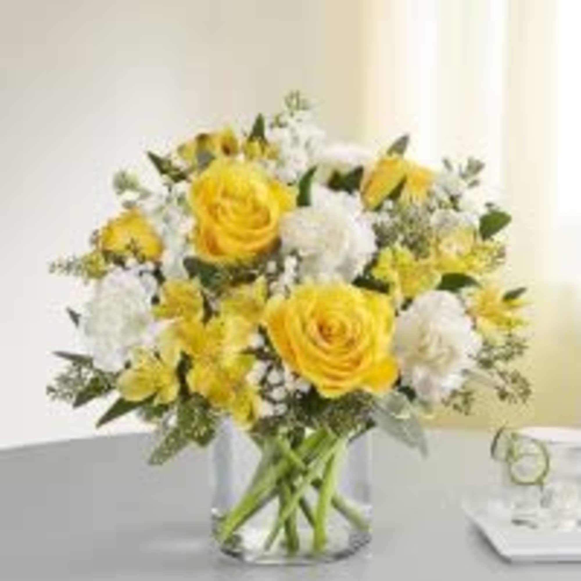 Yellow and white flower arrangement with roses and carnations in a clear glass cylinder vase