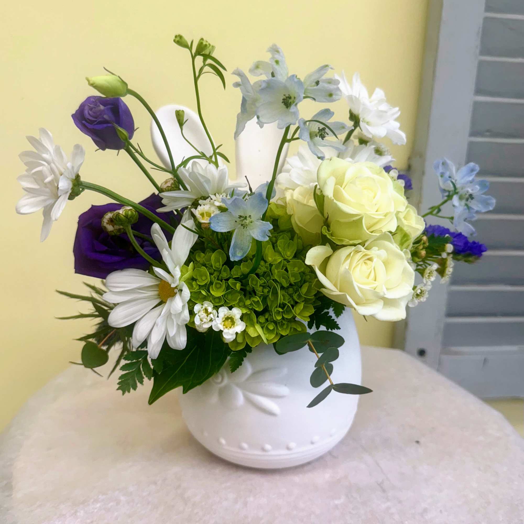 White spray roses, green hydrangeas, blue delphinium, purple lisianthus and white daisies
