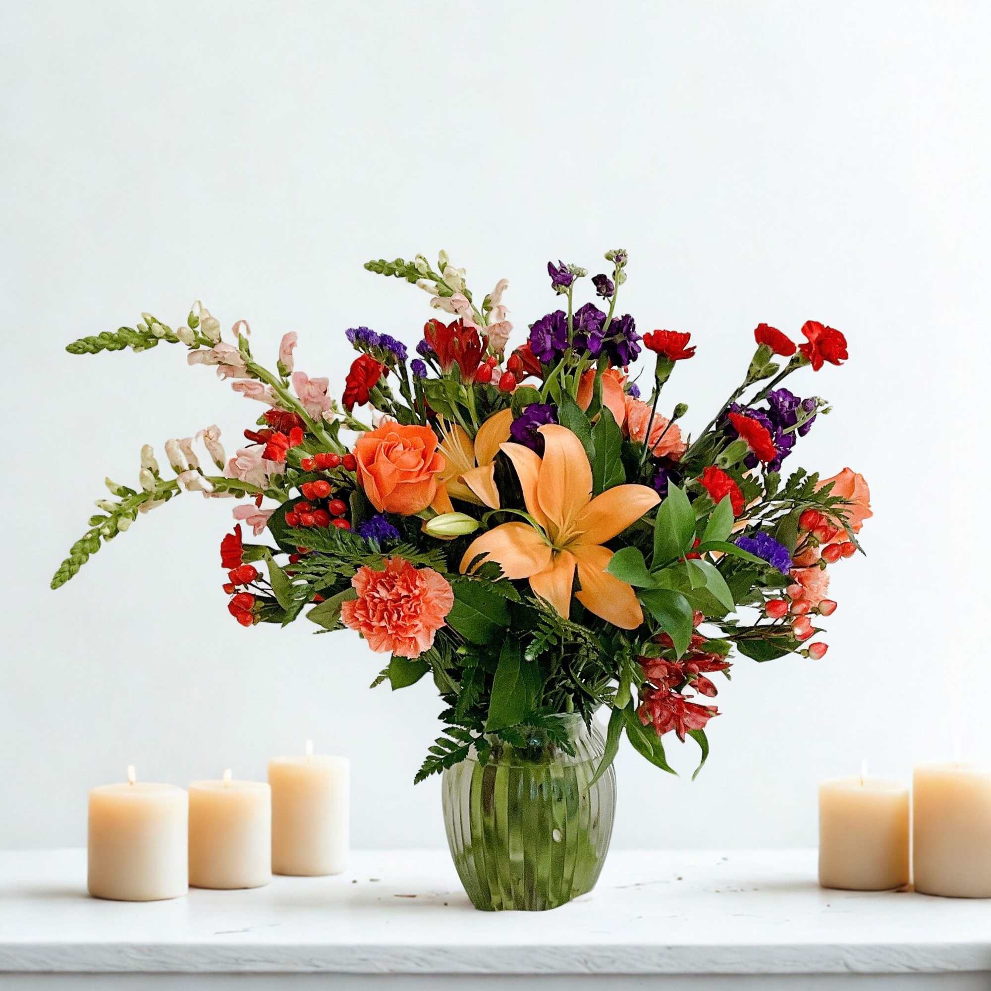 Mixed bouquet of orange, red, and purple flowers in a green glass vase