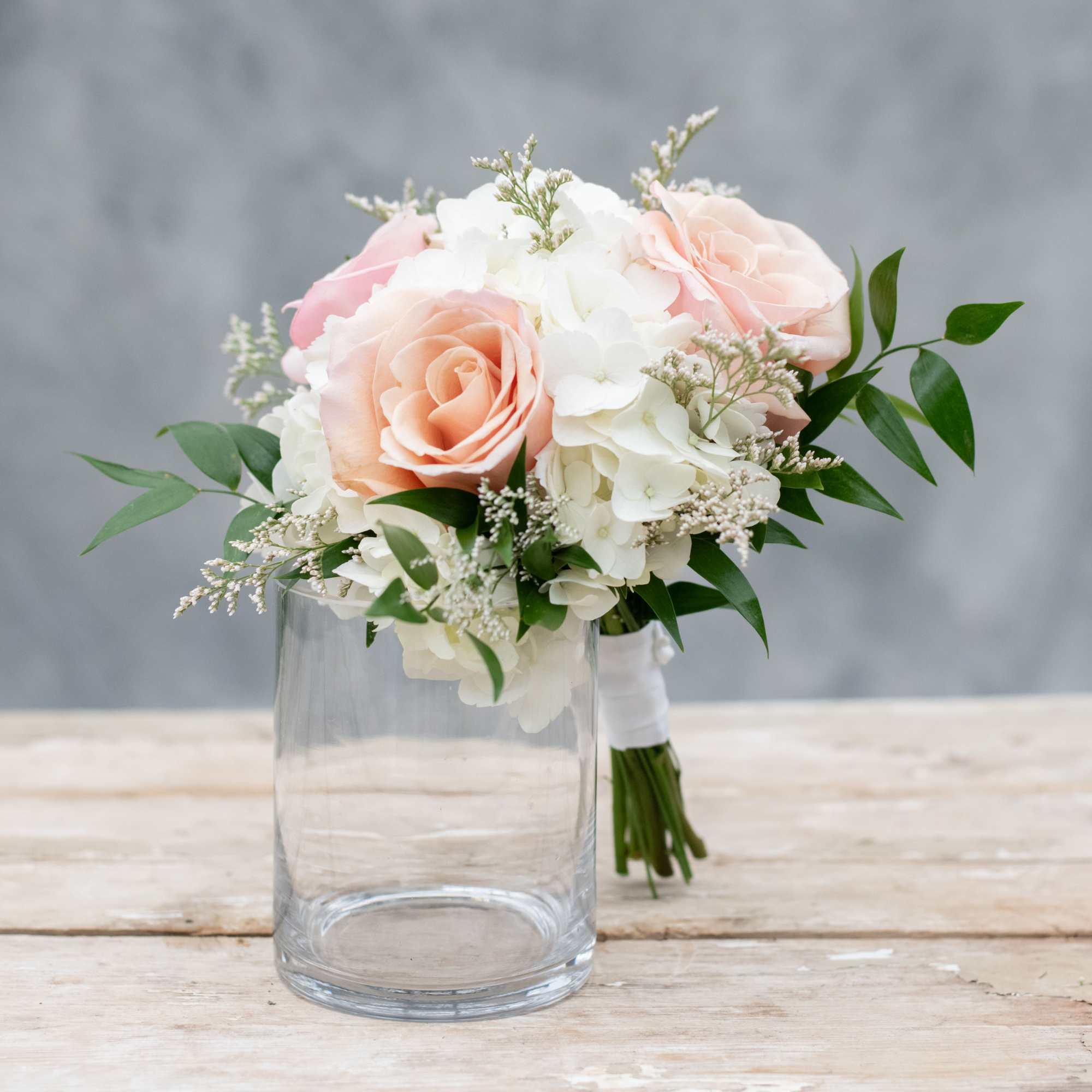 Hand-tied bouquet of peach roses and white hydrangeas resting on a clear glass vase