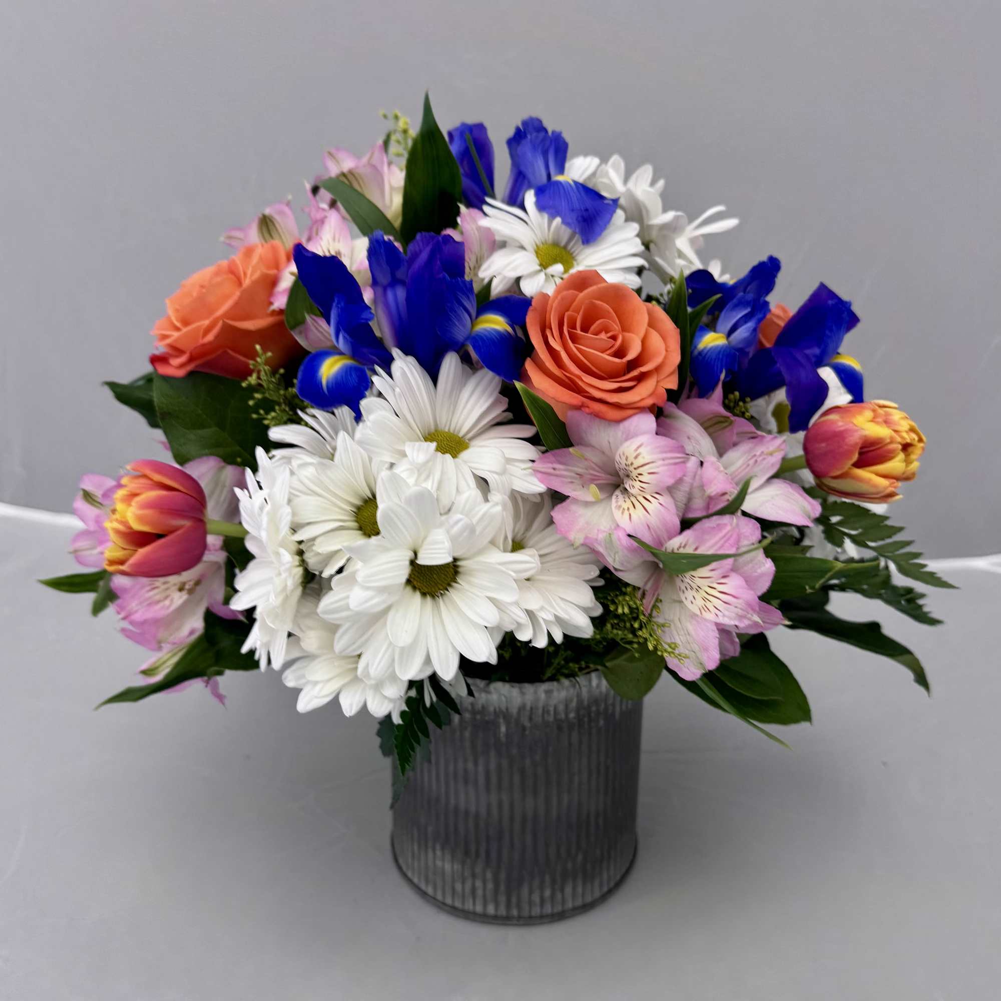 Mixed bouquet of daisies, roses, tulips, and alstroemeria in a metal vase