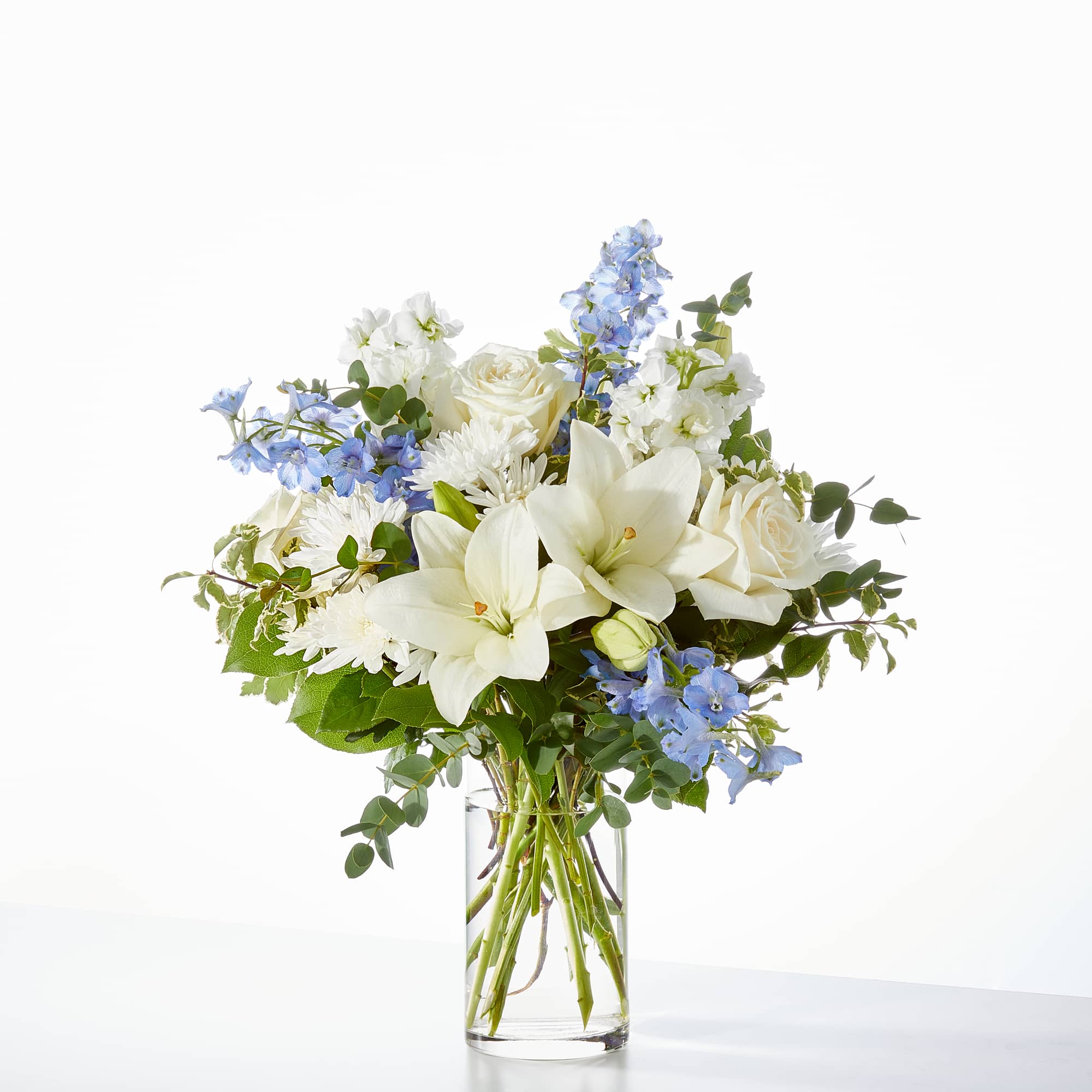 White roses, delicate delphinium, and blooming lilies come together for a luxurious