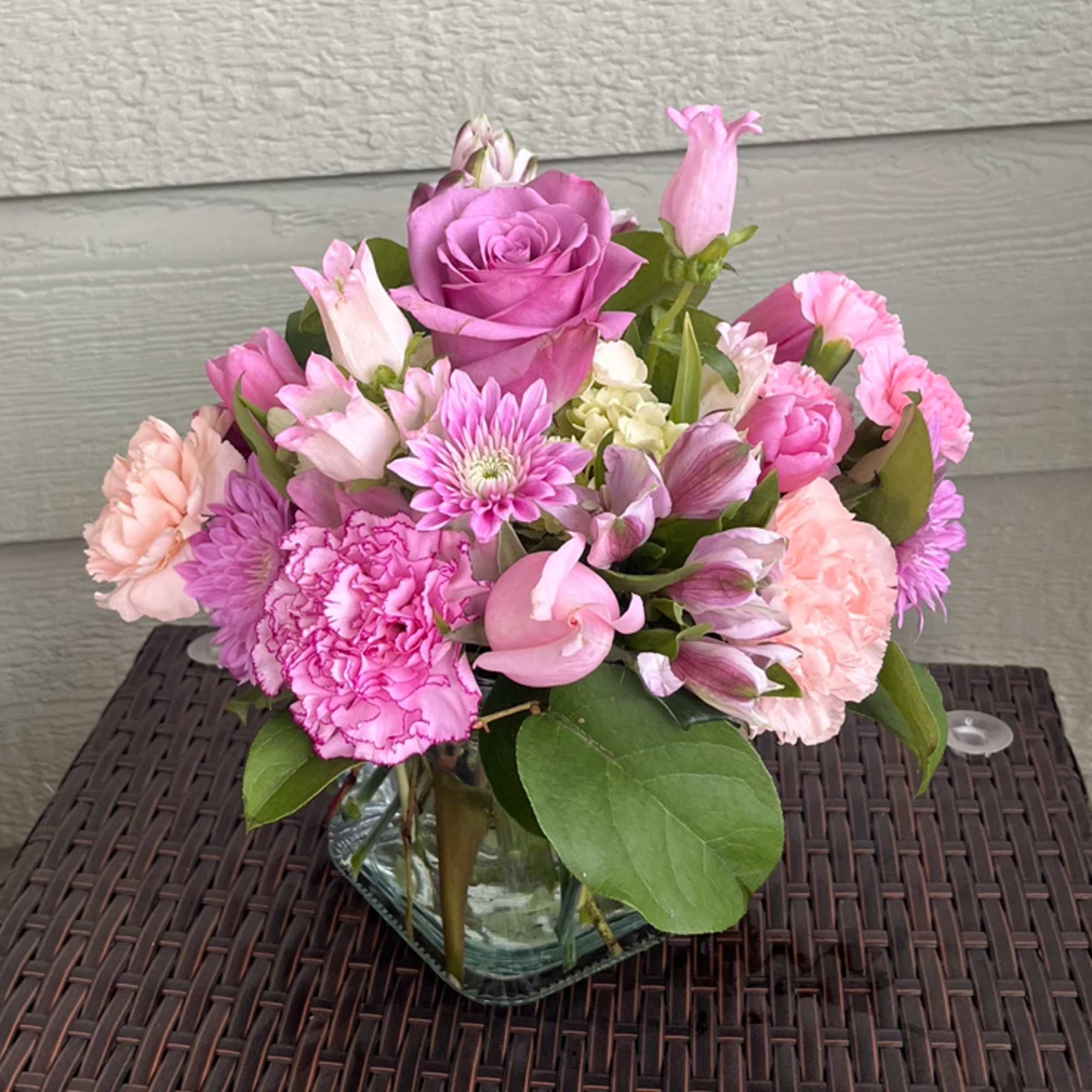 Compact arrangement of pink and lavender flowers in a clear glass cube vase