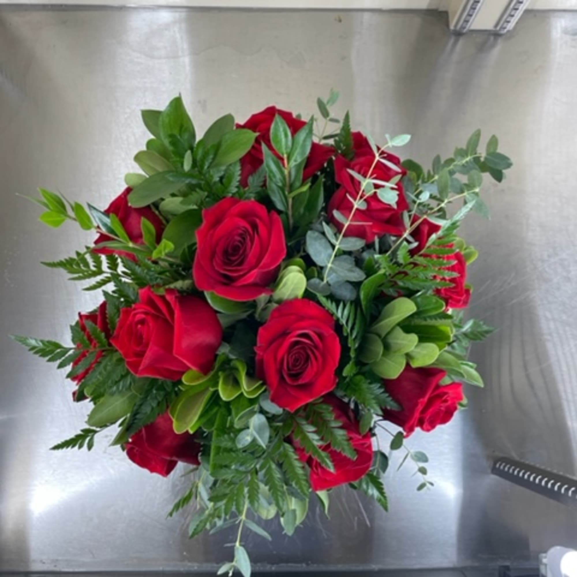 Red roses with mixed greens in a glass vase.