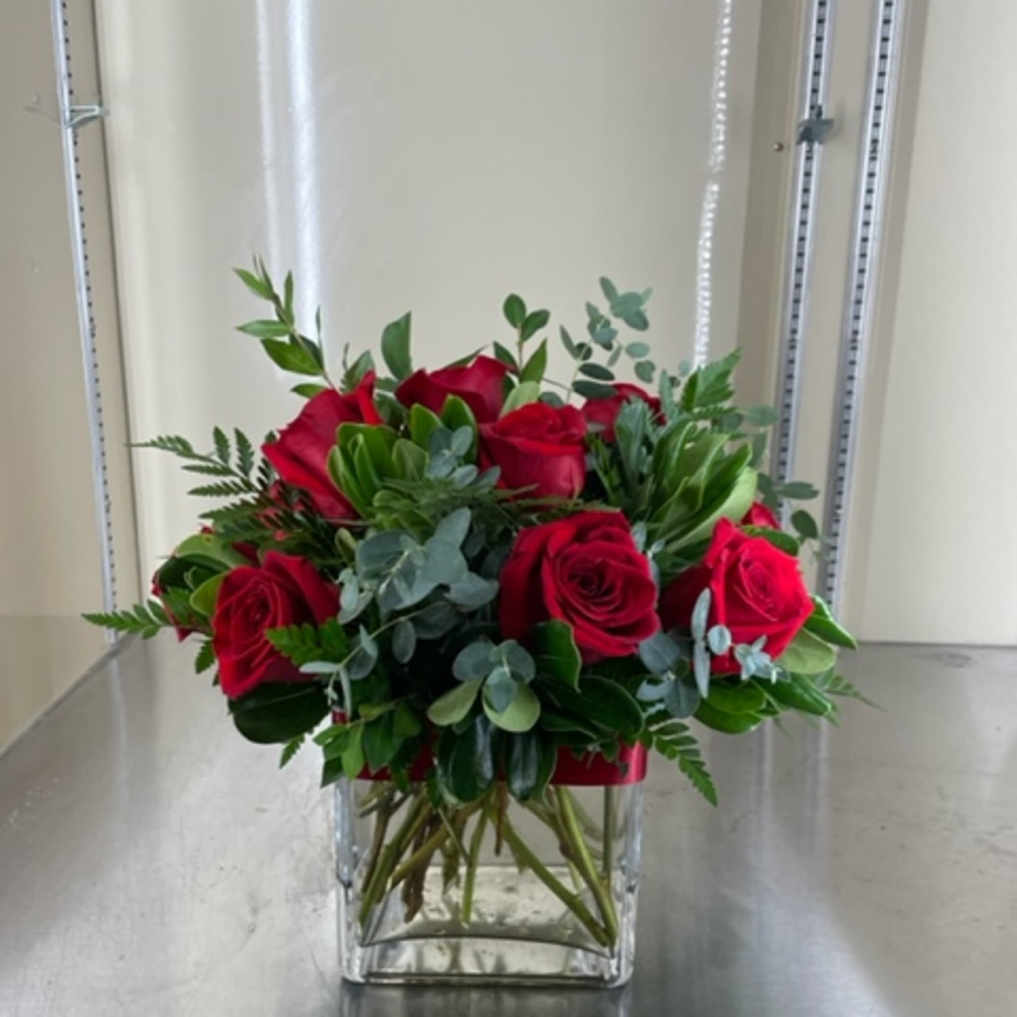 Red roses with mixed greens in a glass vase.