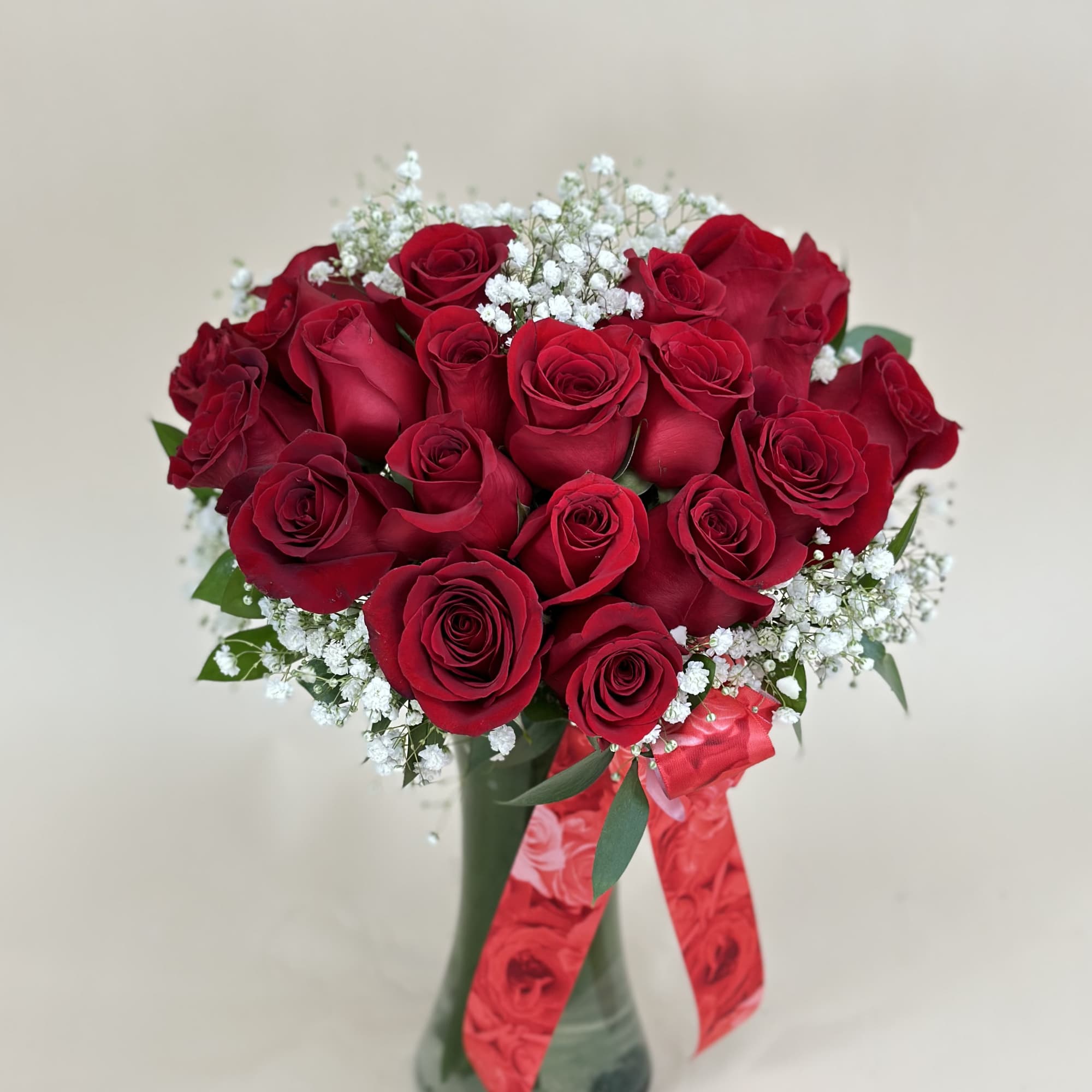 Arrangement of red roses with white filler flowers in a glass vase with a red ribbon