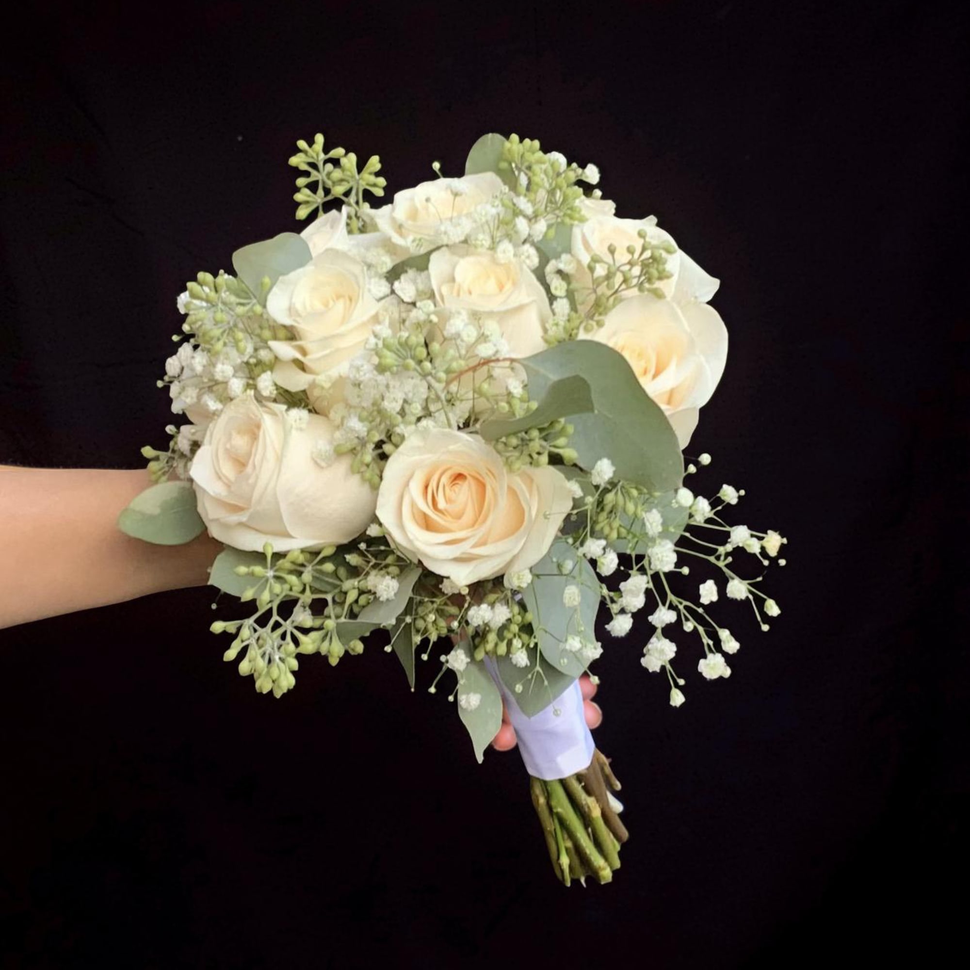 A soft and elegant hand-tied bouquet featuring creamy ivory roses, delicate baby&rsquo;s