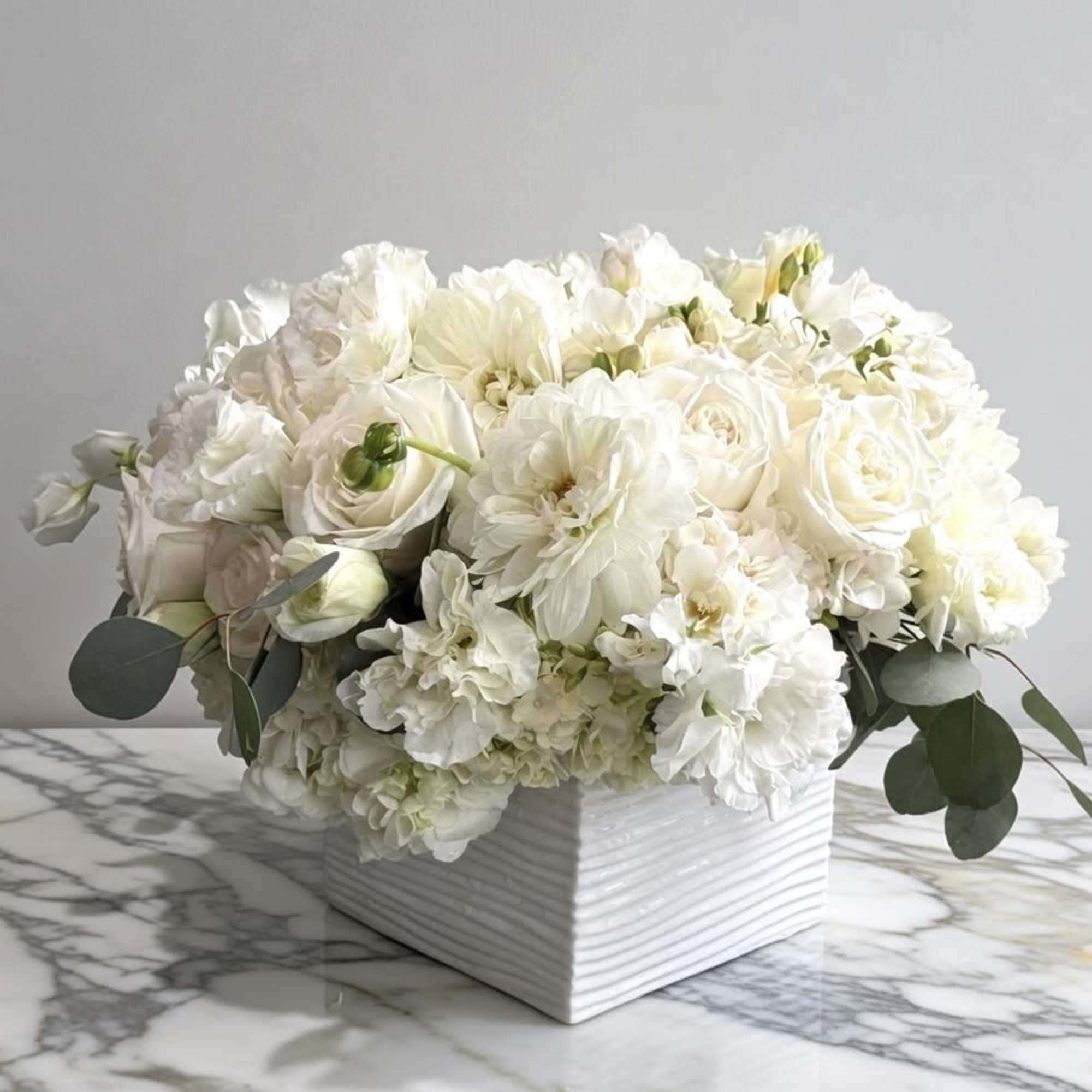 White floral arrangement in a square ceramic vase with eucalyptus accents