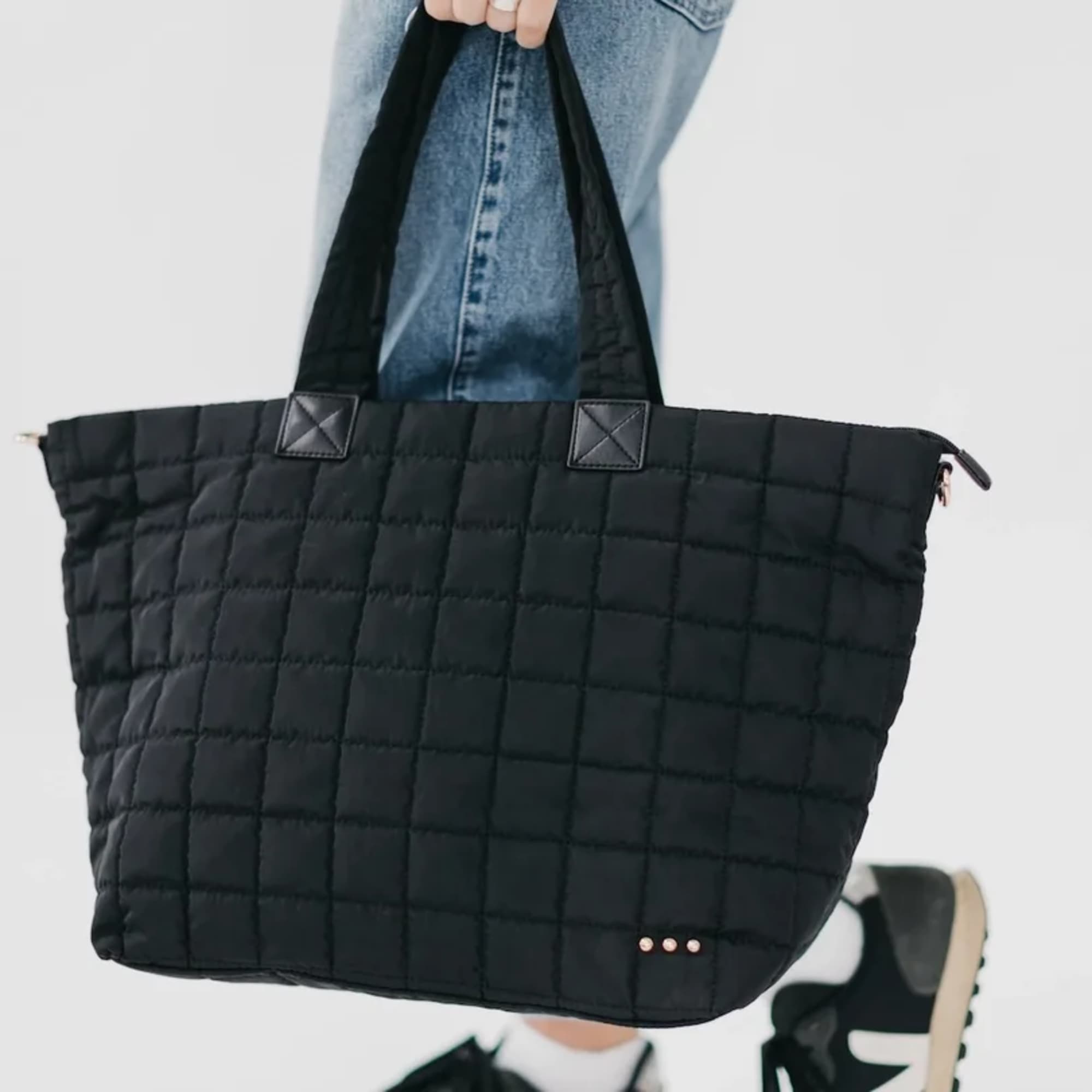 Person holding a large black quilted tote bag by its handles