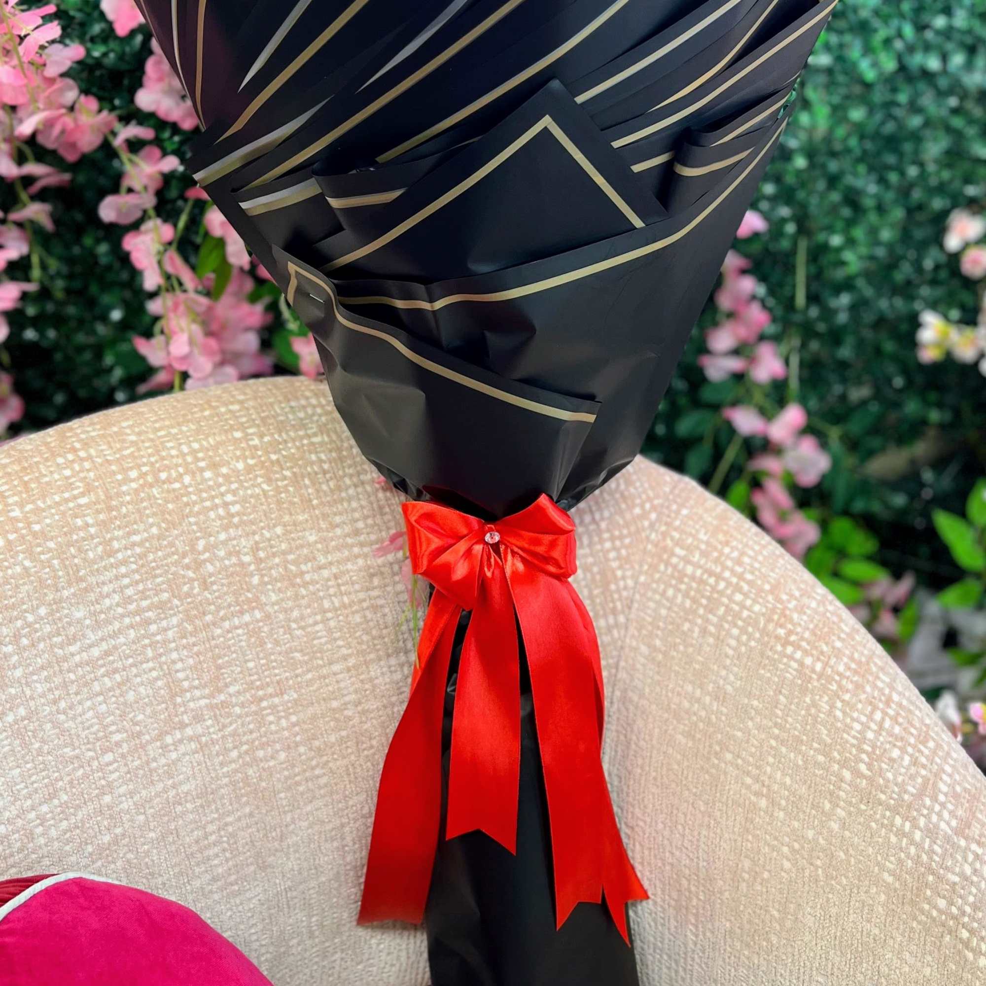 Tall bouquet wrapped in black paper with gold trim and a red satin bow, flowers hidden inside