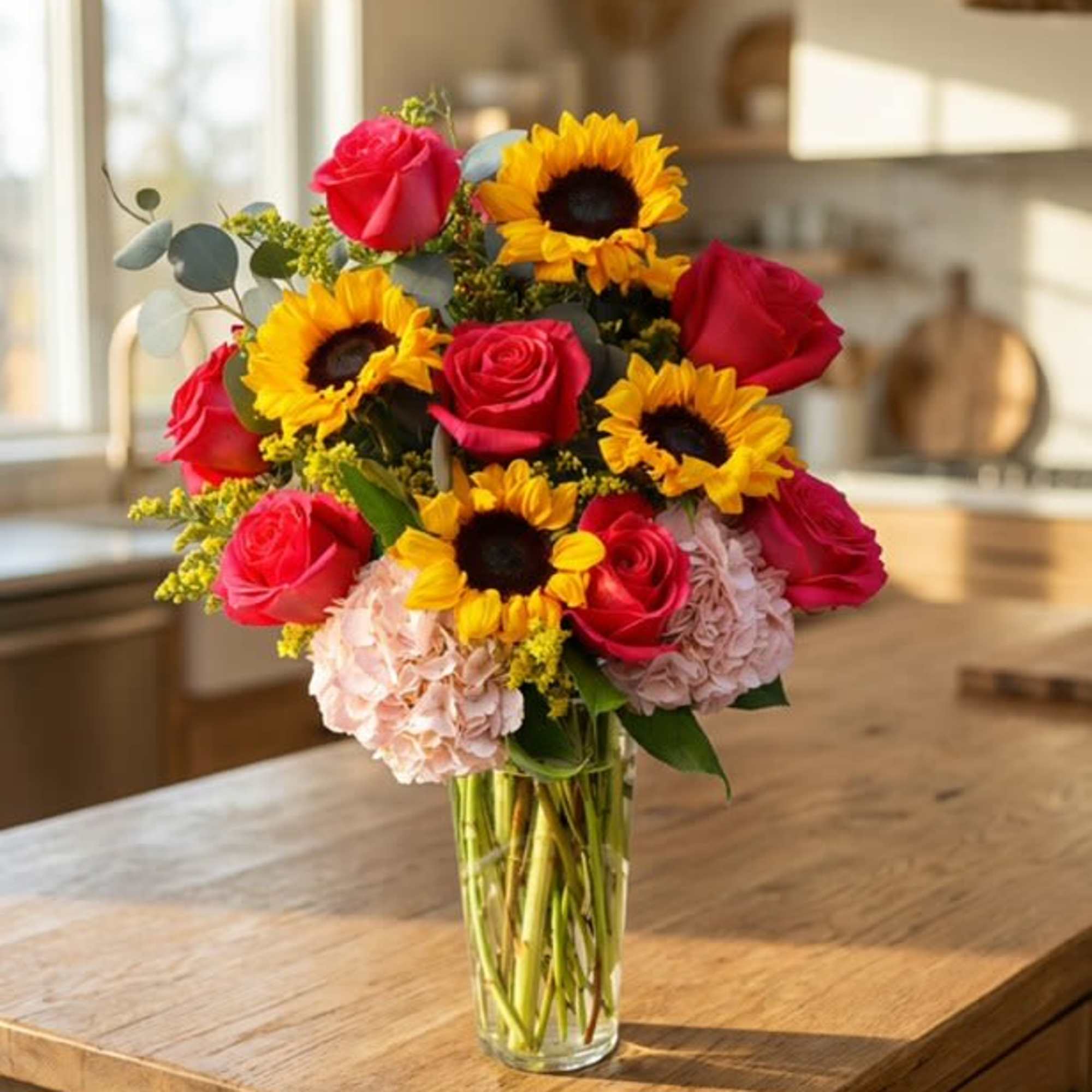 Tall glass vase of yellow sunflowers, hot pink roses, and soft pink hydrangeas on a wooden kitchen island