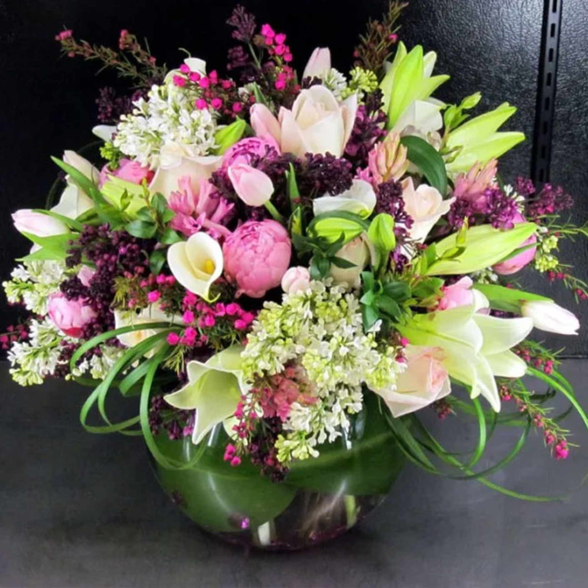 Round arrangement of pink and white lilies, peonies, roses and calla lilies in a clear glass bowl vase