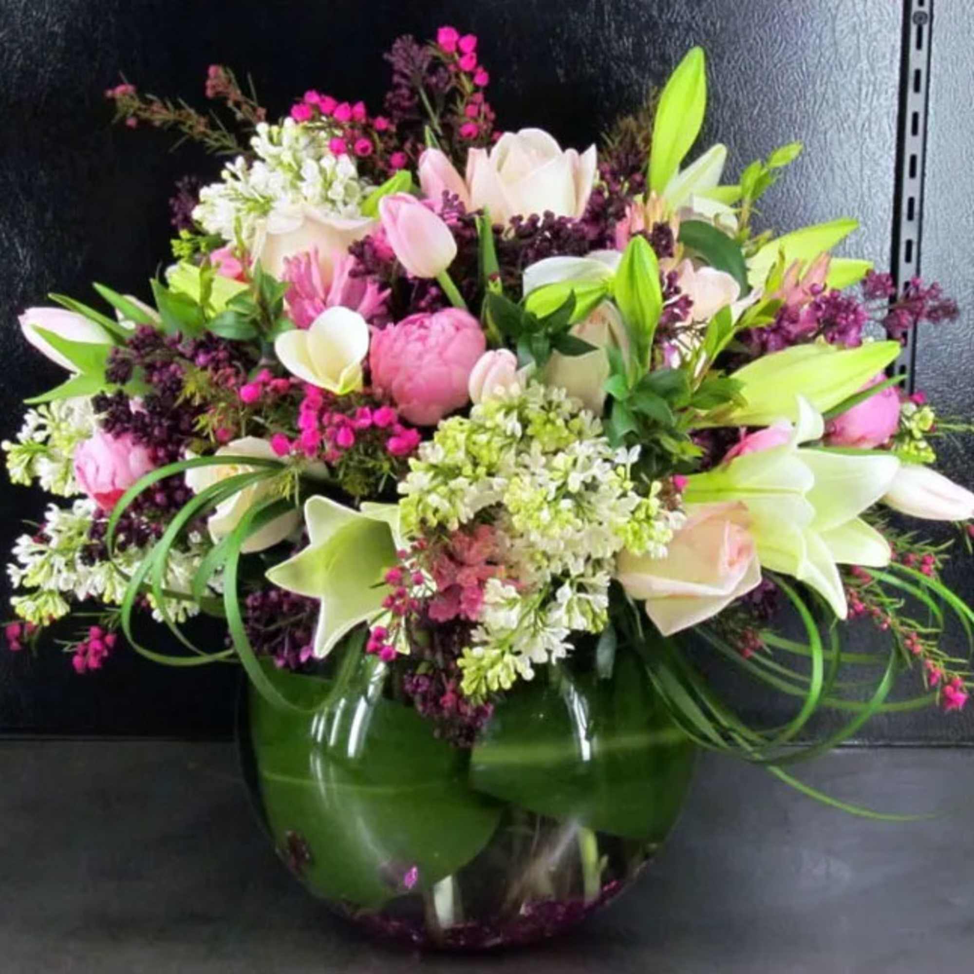 Mixed arrangement of pink and white flowers in a round clear glass vase.