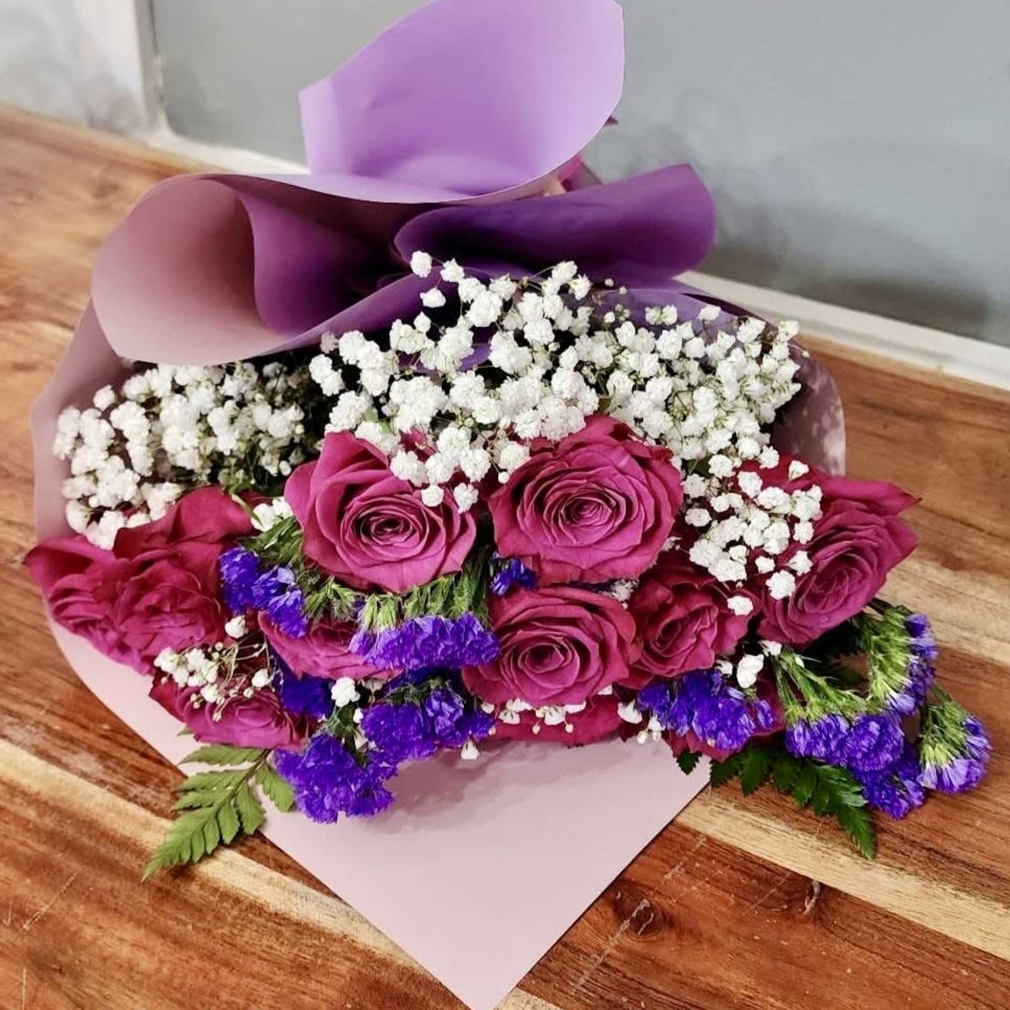 Bouquet of magenta roses with white filler flowers and purple accents wrapped in pink and lavender paper