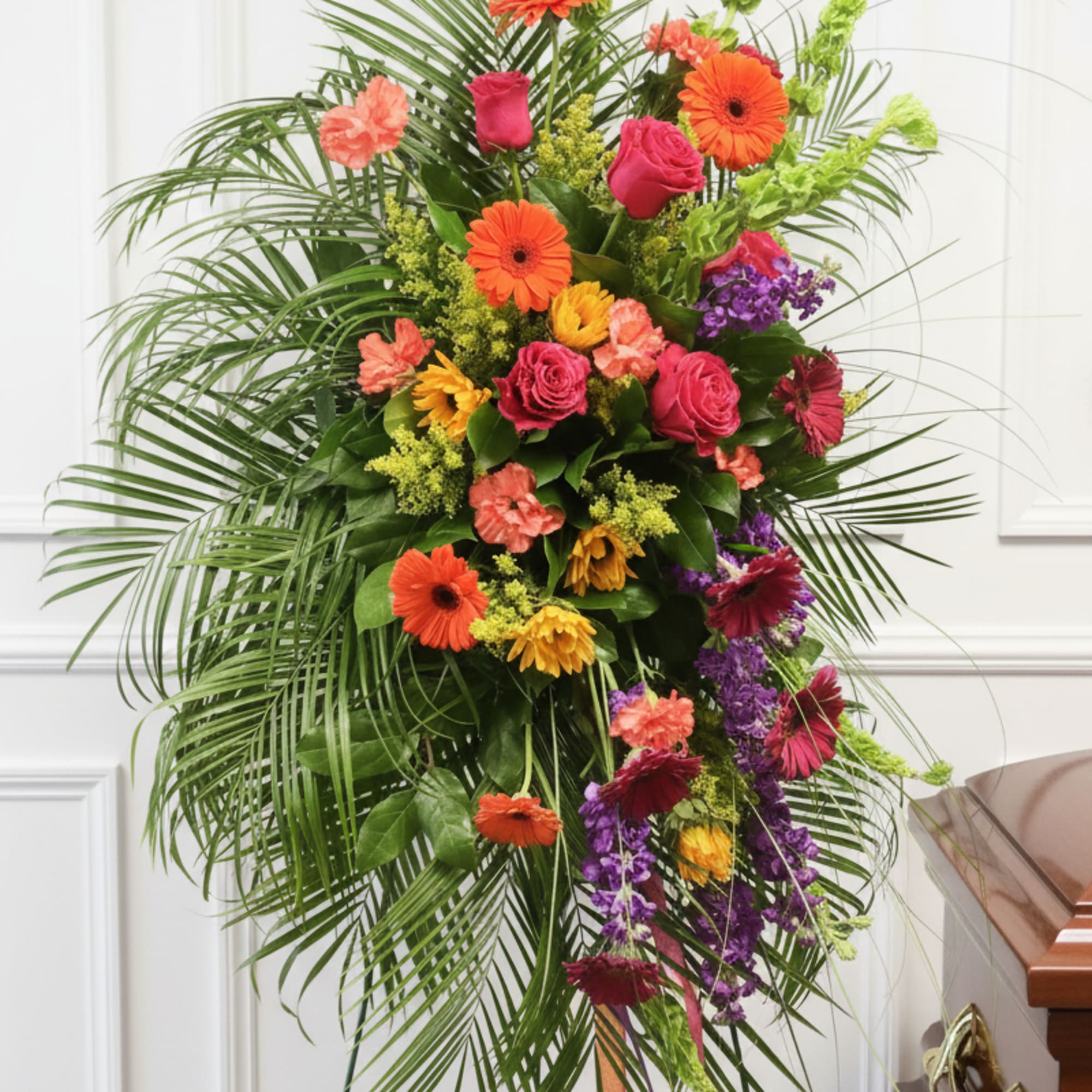 Tall standing spray with bright orange gerberas, pink roses, and purple flowers on an easel
