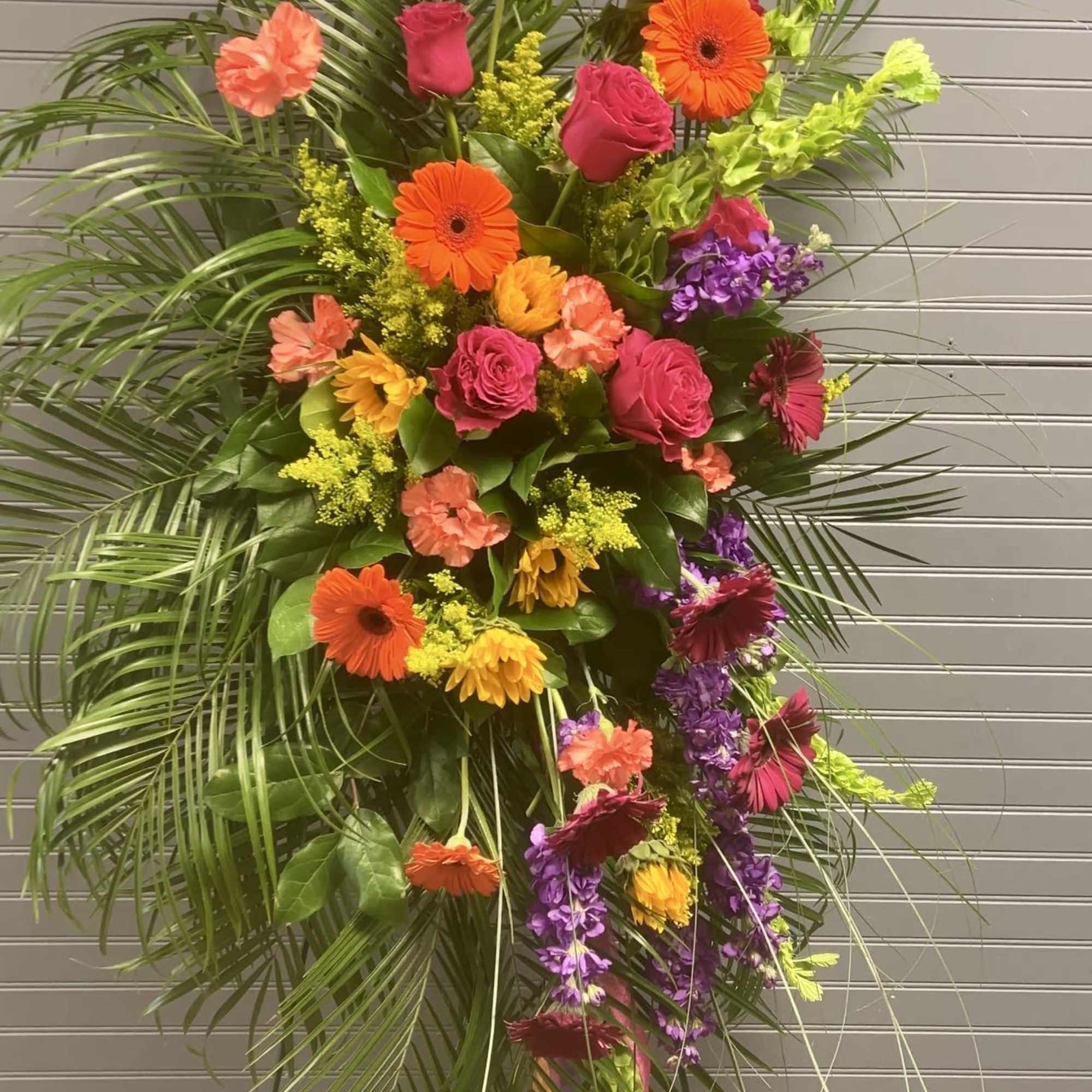 Tall standing spray with bright orange gerberas, pink roses, and mixed blooms on a metal easel