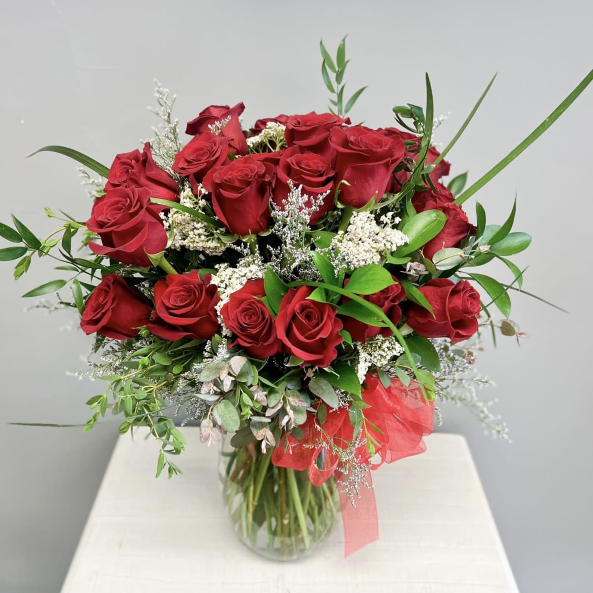 12 Red roses accented with premium greens in a  clear vase.