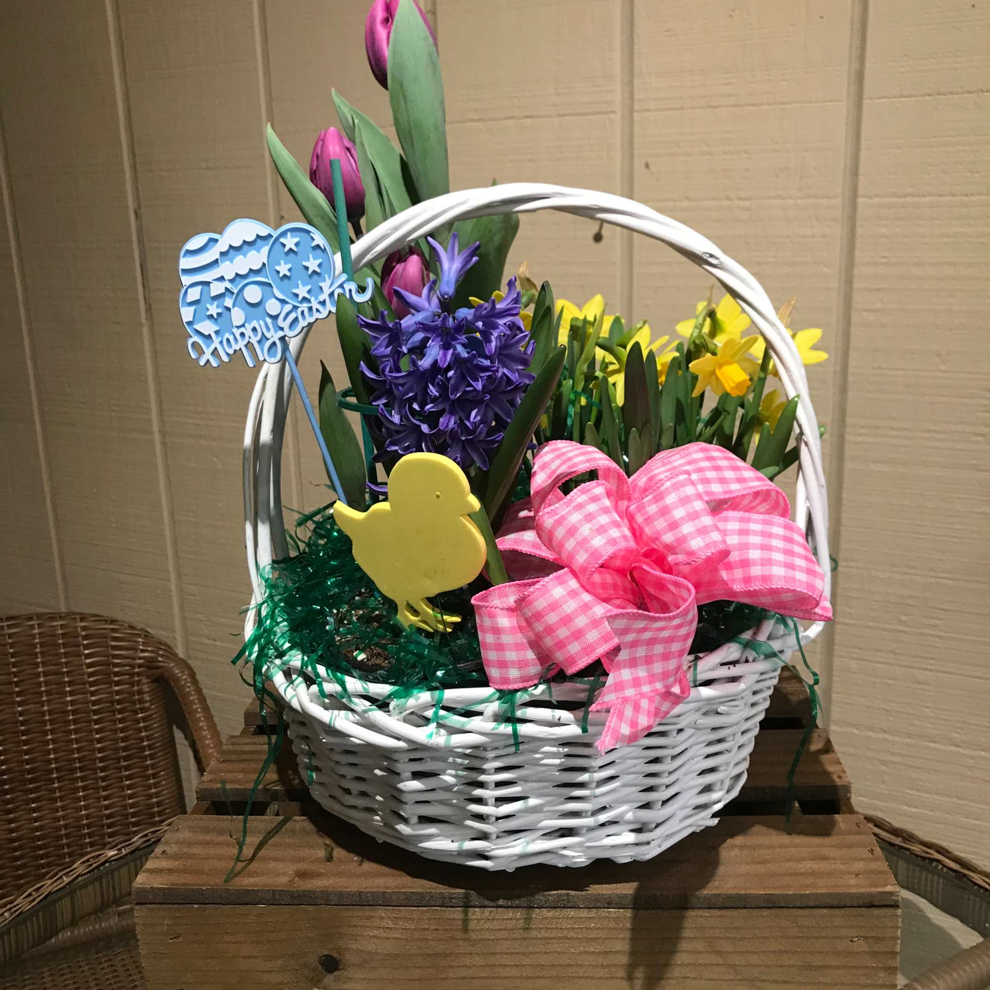 White basket with purple tulips, hyacinth, and yellow daffodils arranged with Easter decorations.