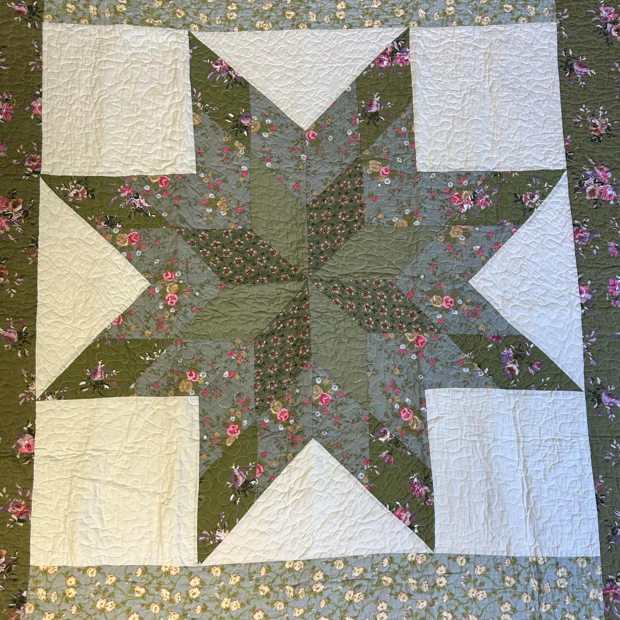 Green and cream patchwork quilt with a large central star and floral print fabrics