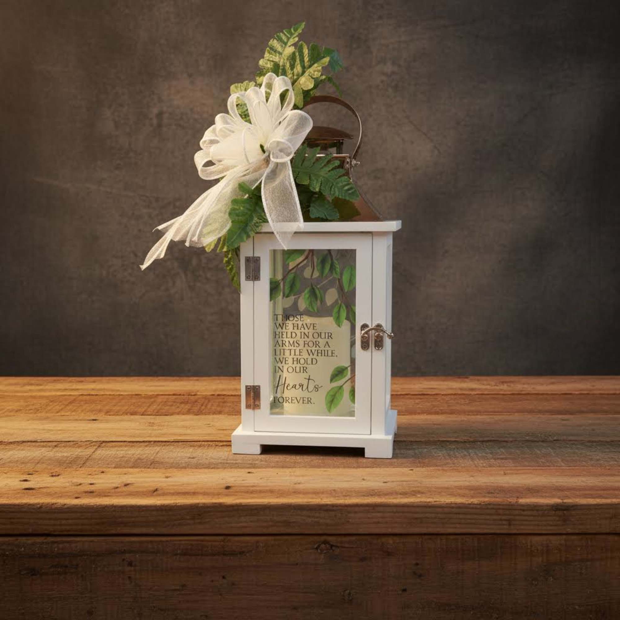 White memorial lantern with printed verse, topped with a white bow and green foliage.