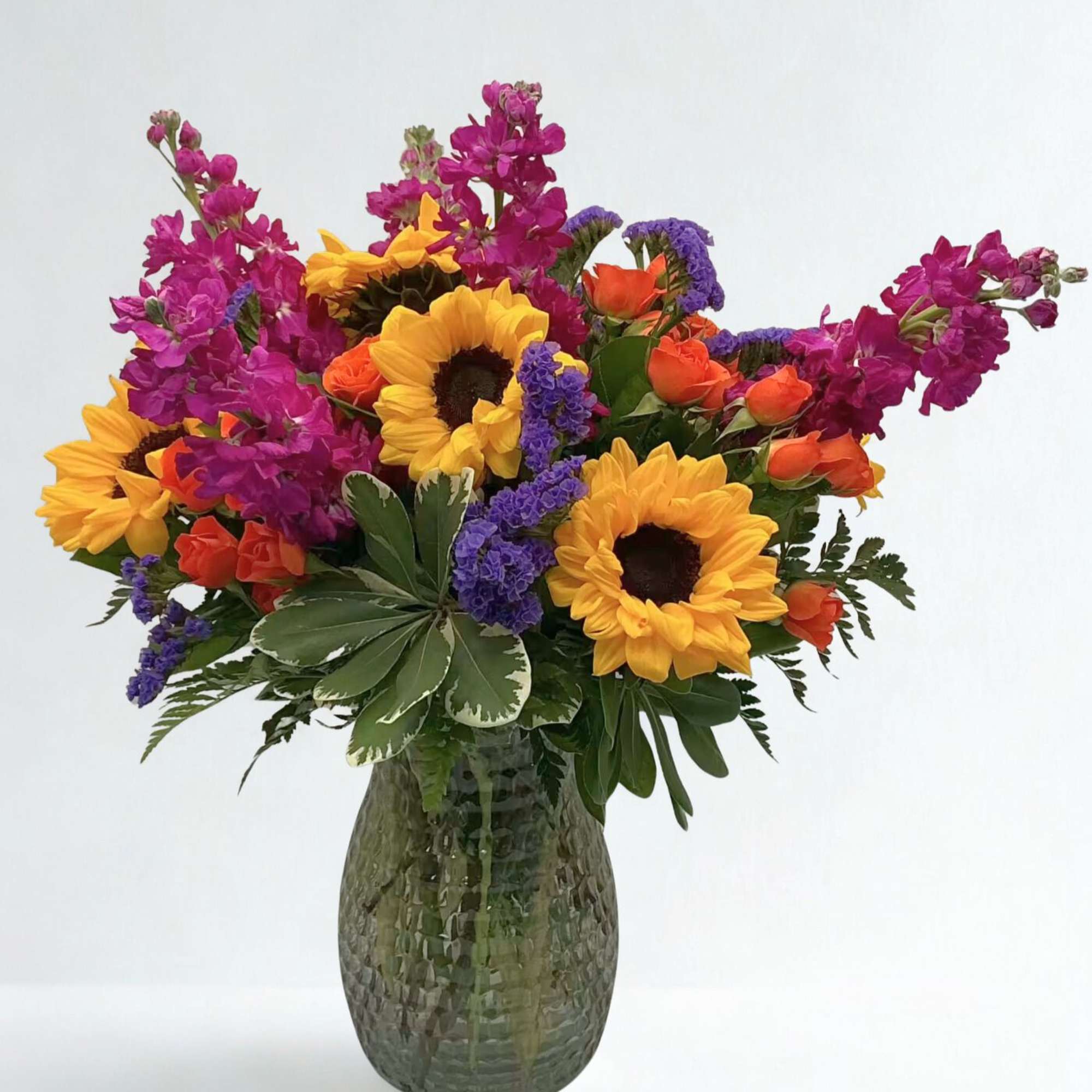 Colorful bouquet with sunflowers, orange roses, and purple flowers in a glass vase