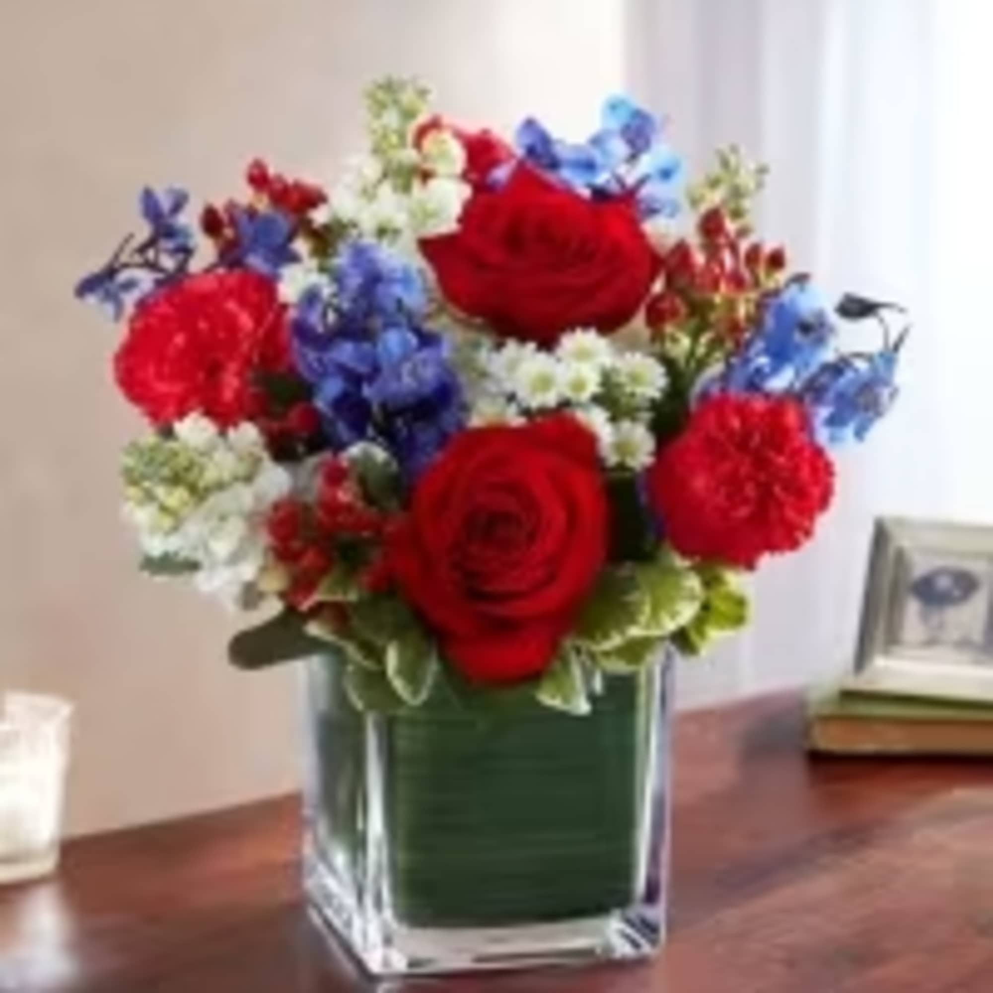 Red, white, and blue flower arrangement with roses and carnations in a clear square glass vase
