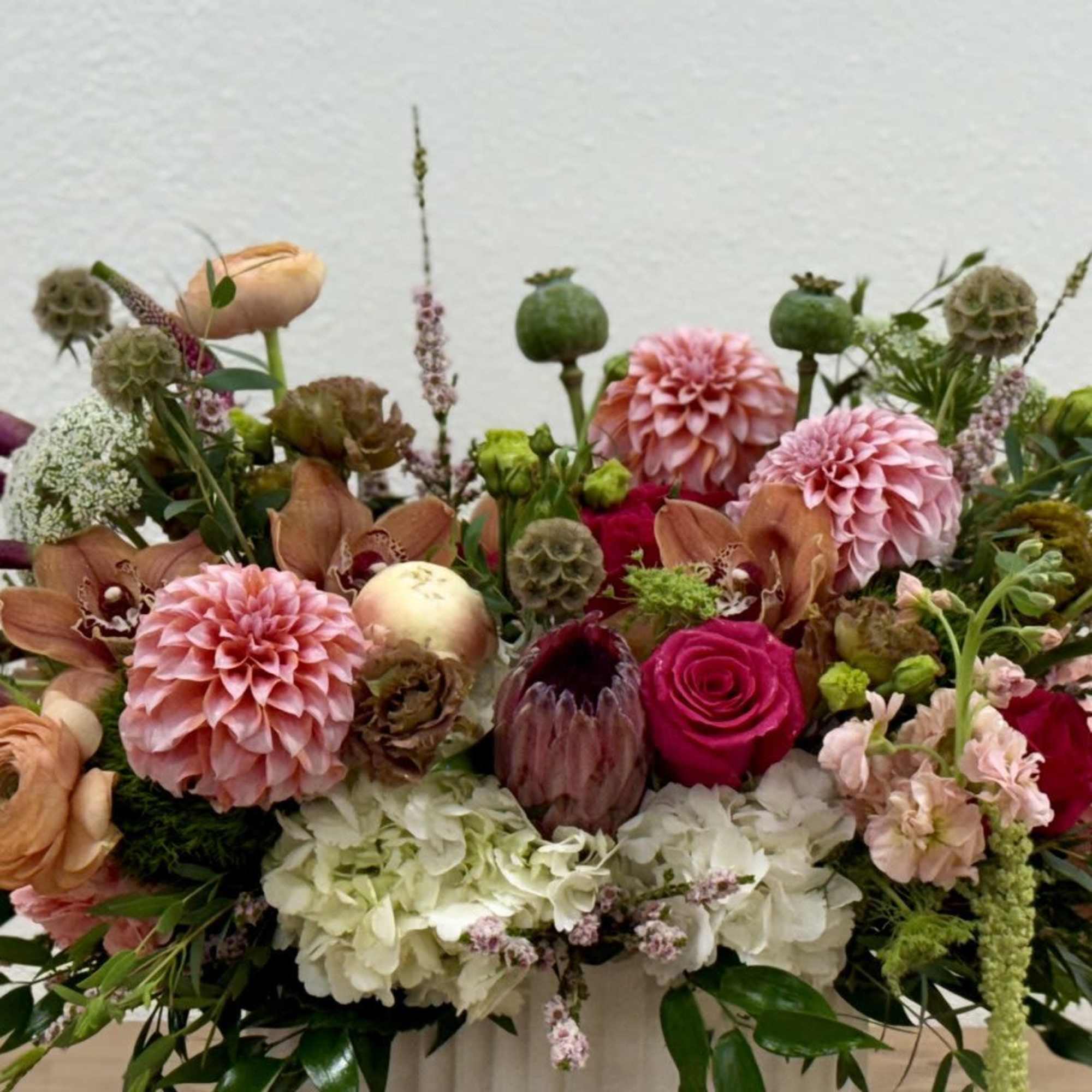 Low centerpiece of pink dahlias, roses, hydrangea and mixed blooms in a white vase