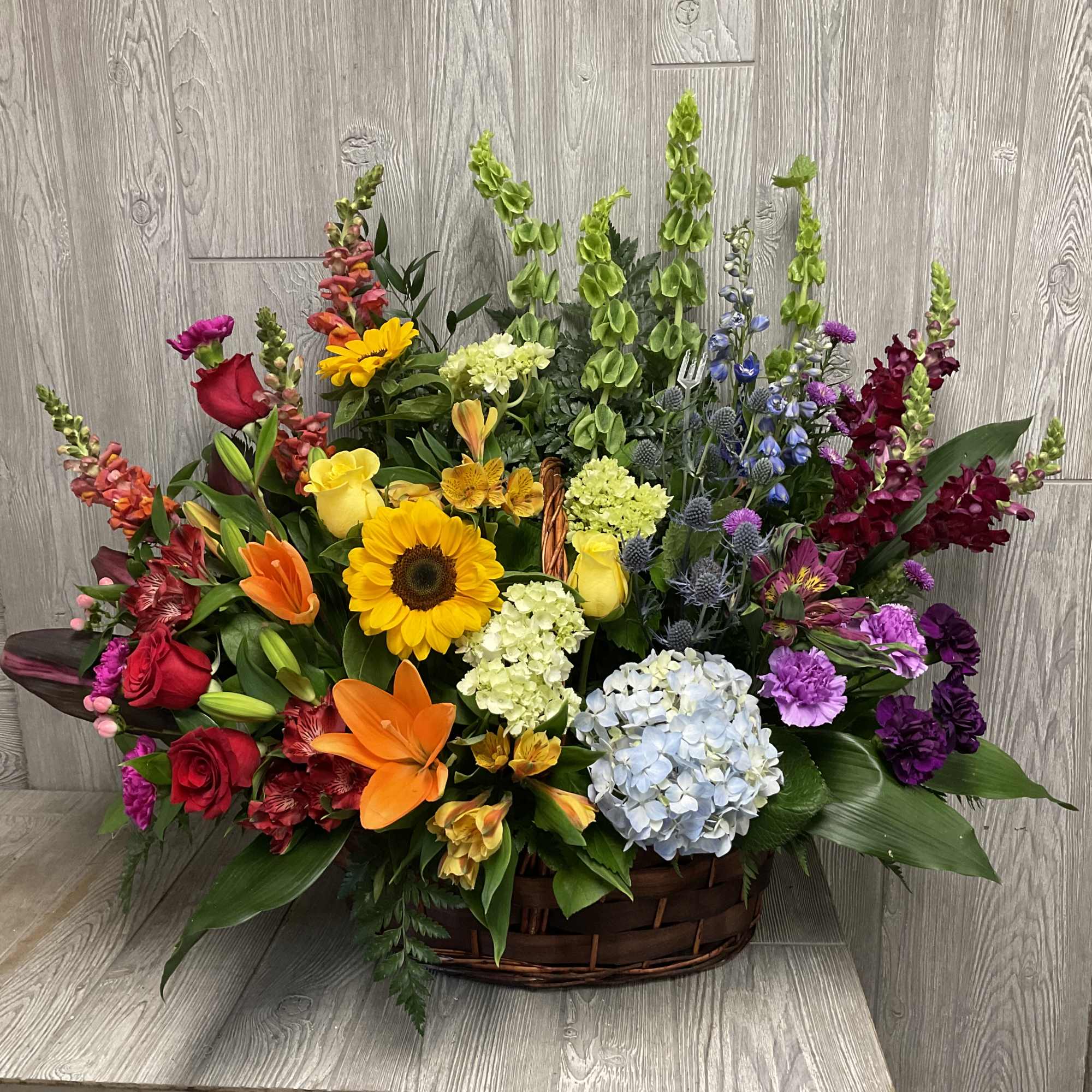 Large mixed basket arrangement of colorful roses, lilies, hydrangeas, sunflowers, snapdragons, and other blooms.