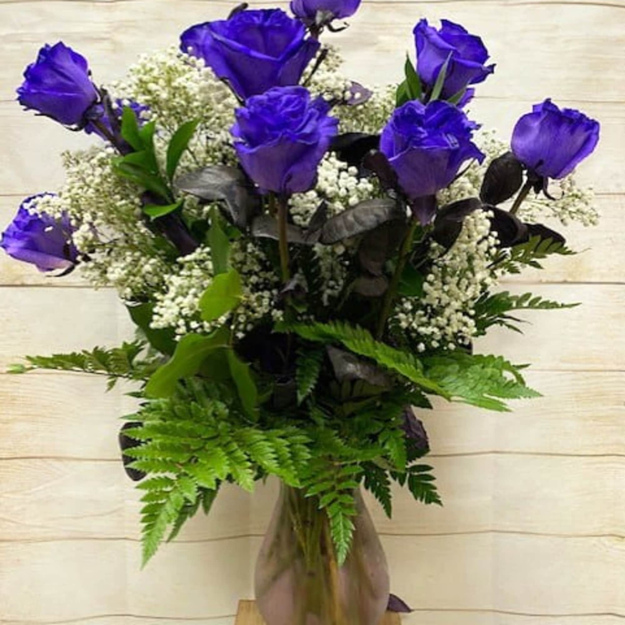 Tall arrangement of vivid blue roses with white filler flowers in a clear glass vase