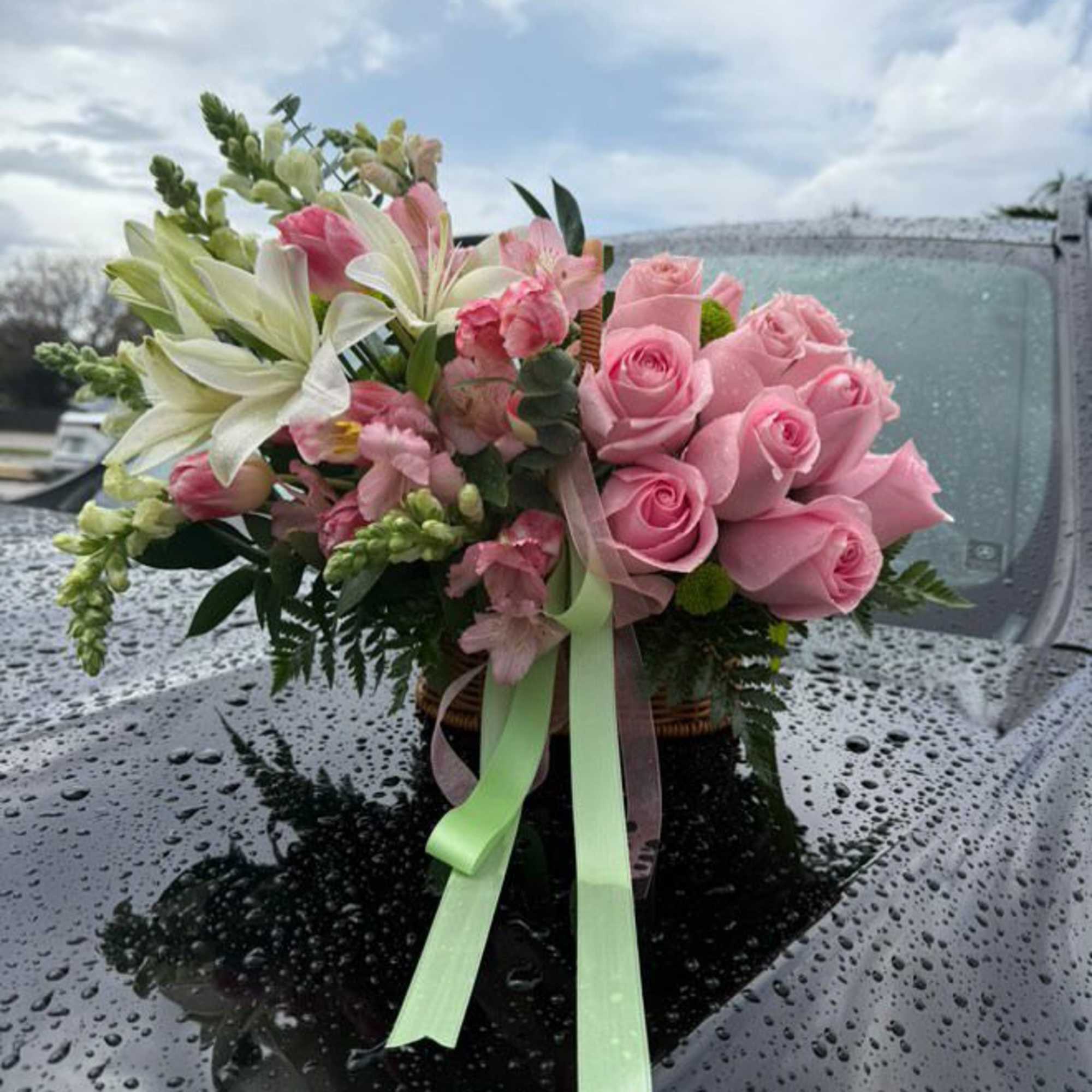 Pink rose and lily bouquet with ribbon on a car hood