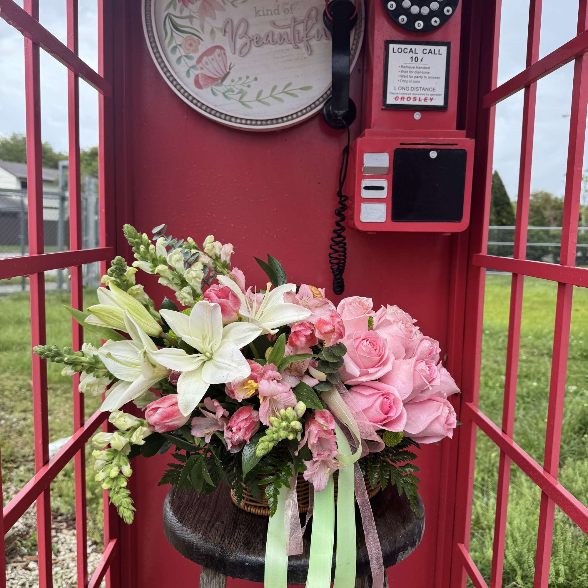 Pink and white flower arrangement in a basket with ribbon streamers