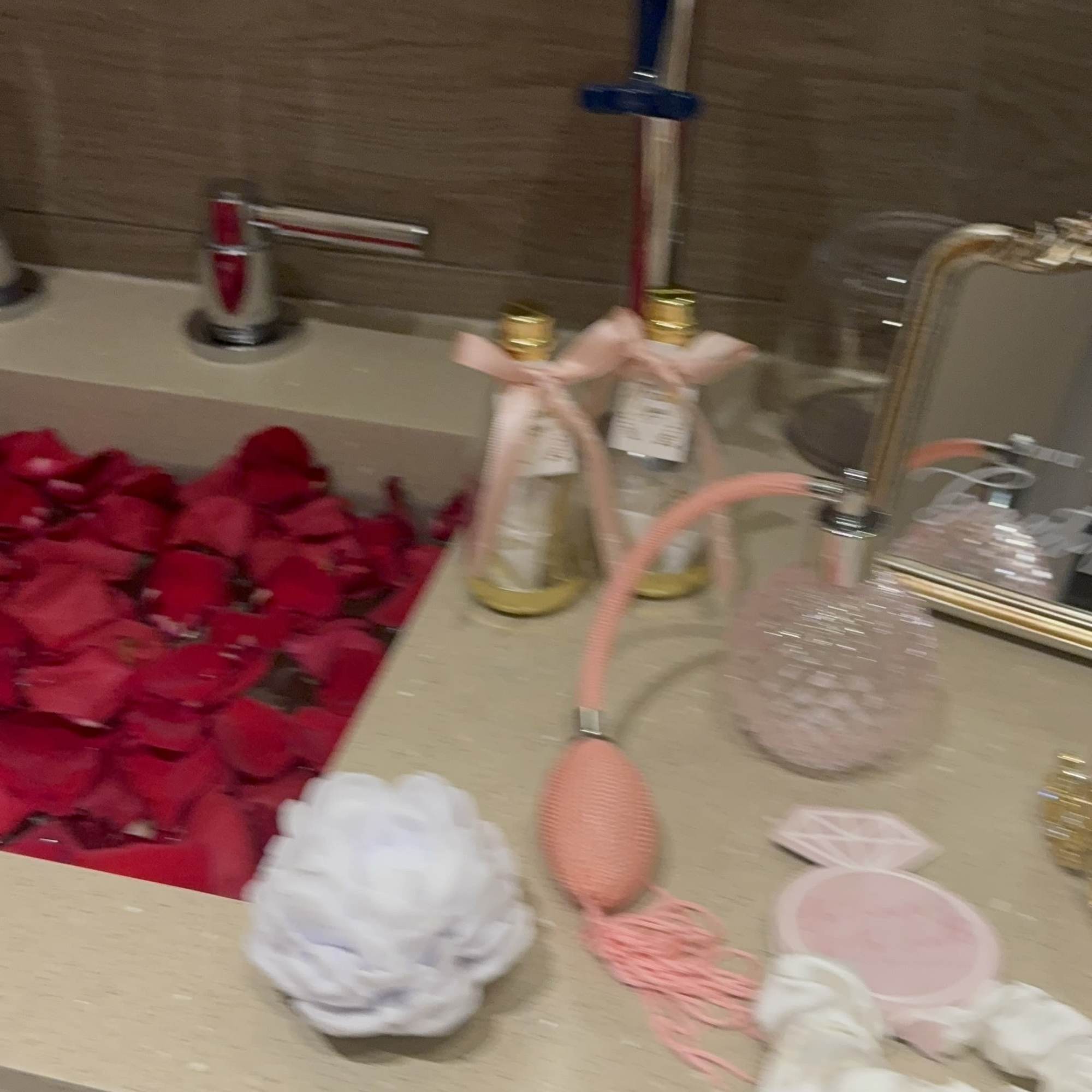 Countertop with scattered red rose petals and decorative bath items
